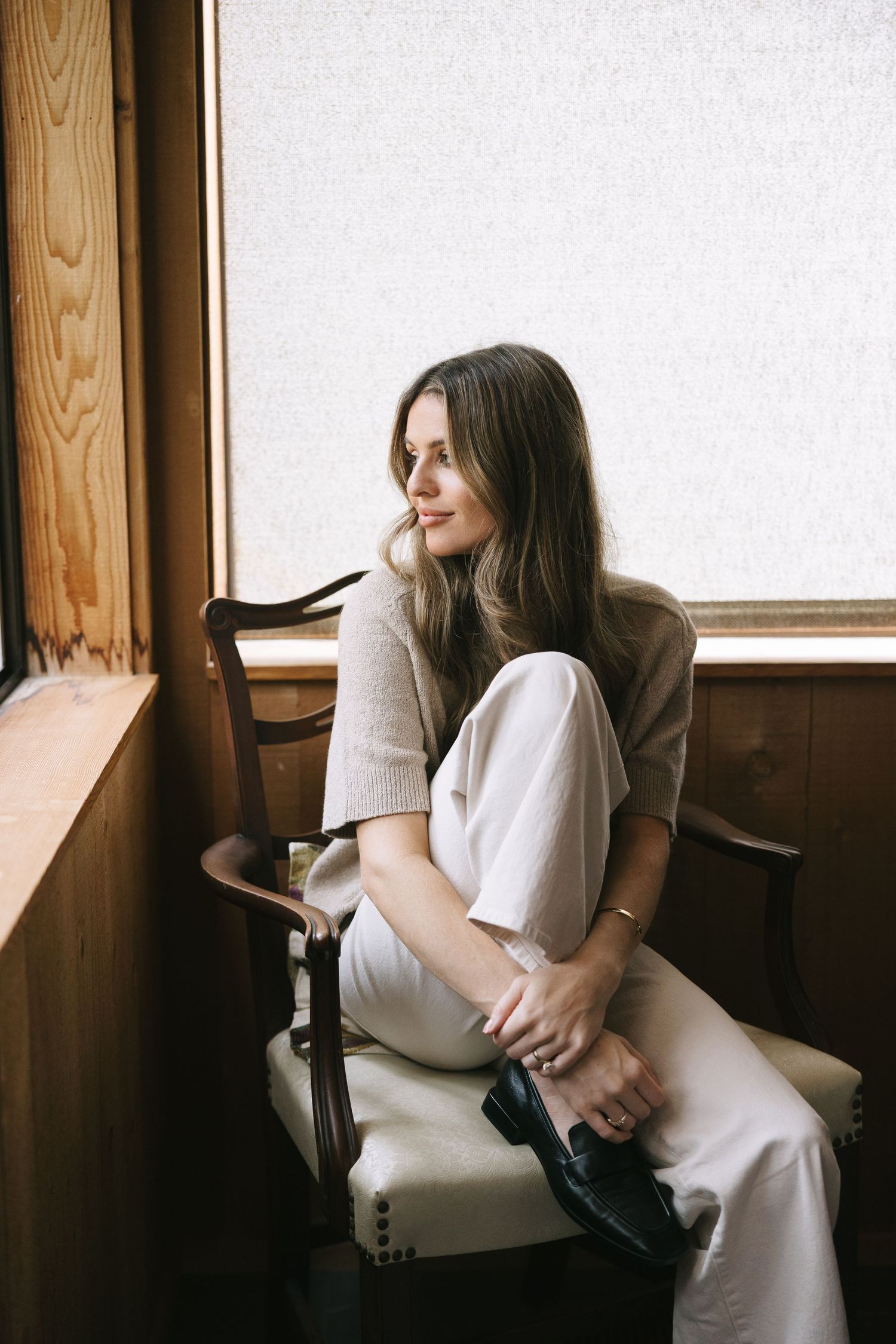 Soft natural light illuminates a person in white sitting by a window in a wooden interior.