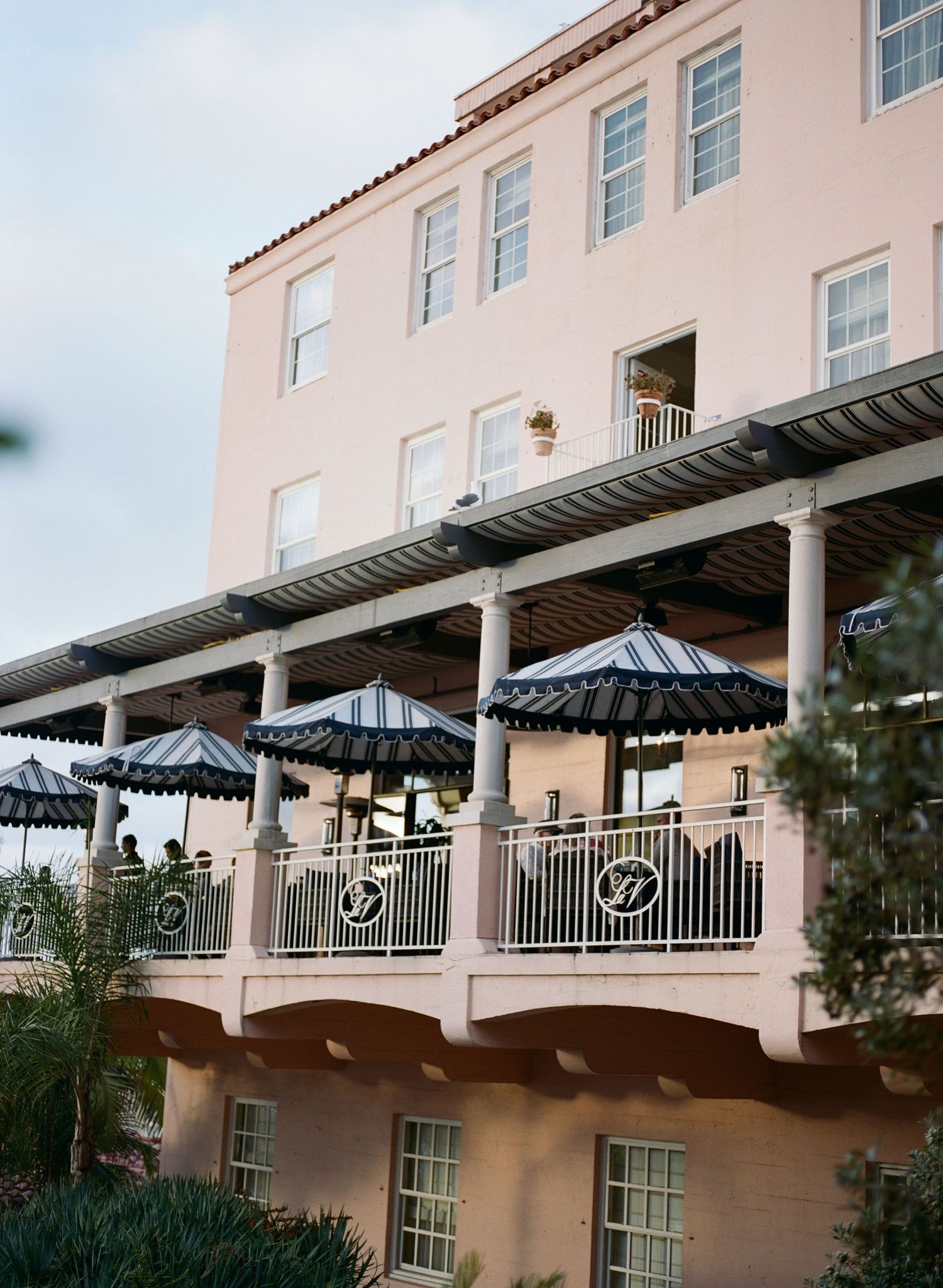 Pink stucco building with white columns and striped awnings on a balcony terrace.