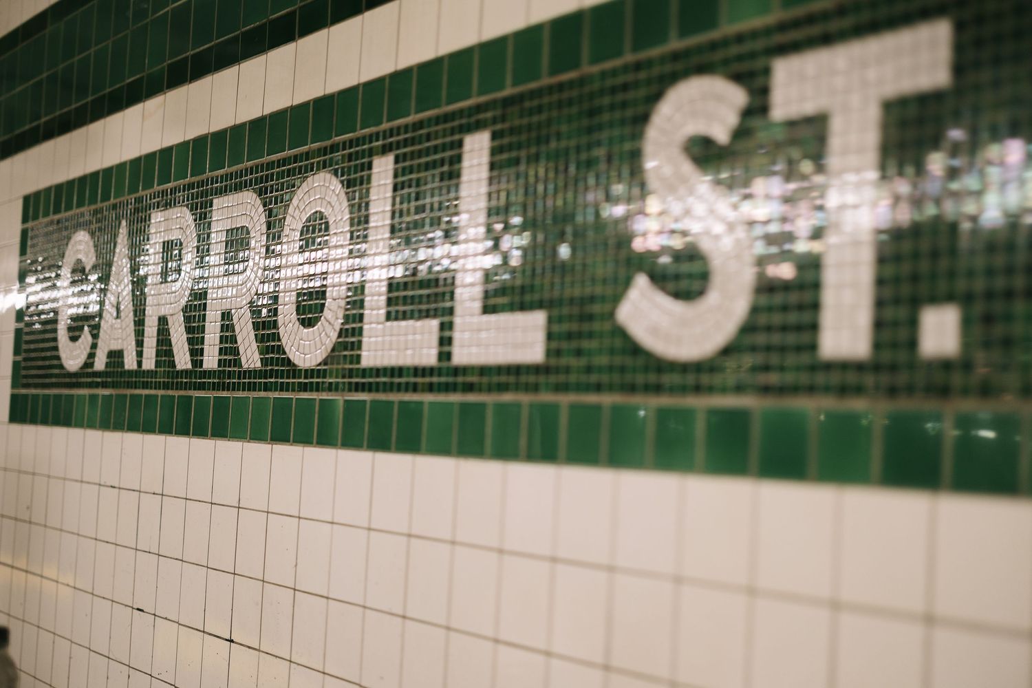 Green tiled subway station wall with text signage visible.