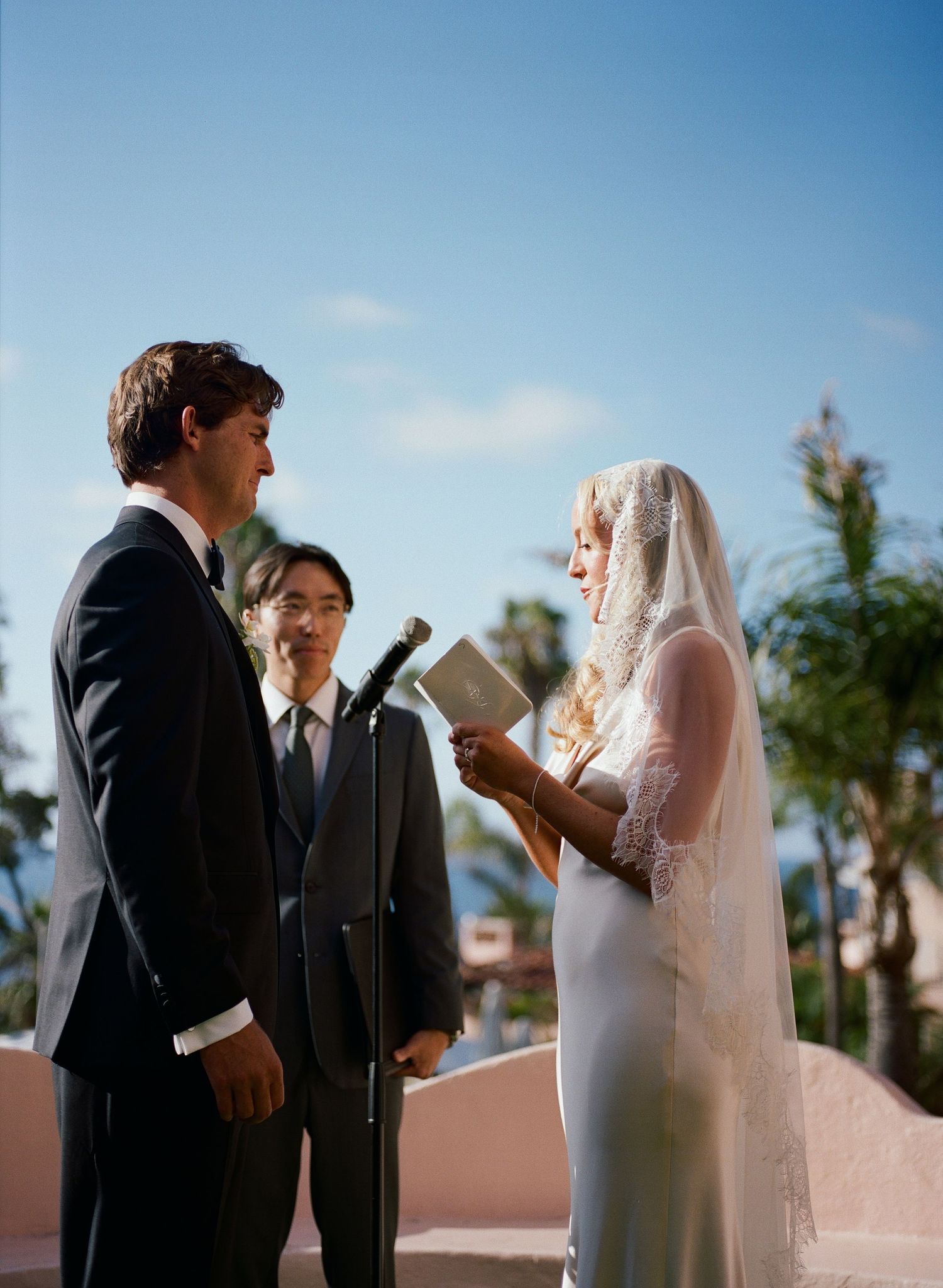 Outdoor wedding ceremony taking place on a sunny day with palm trees in the background.