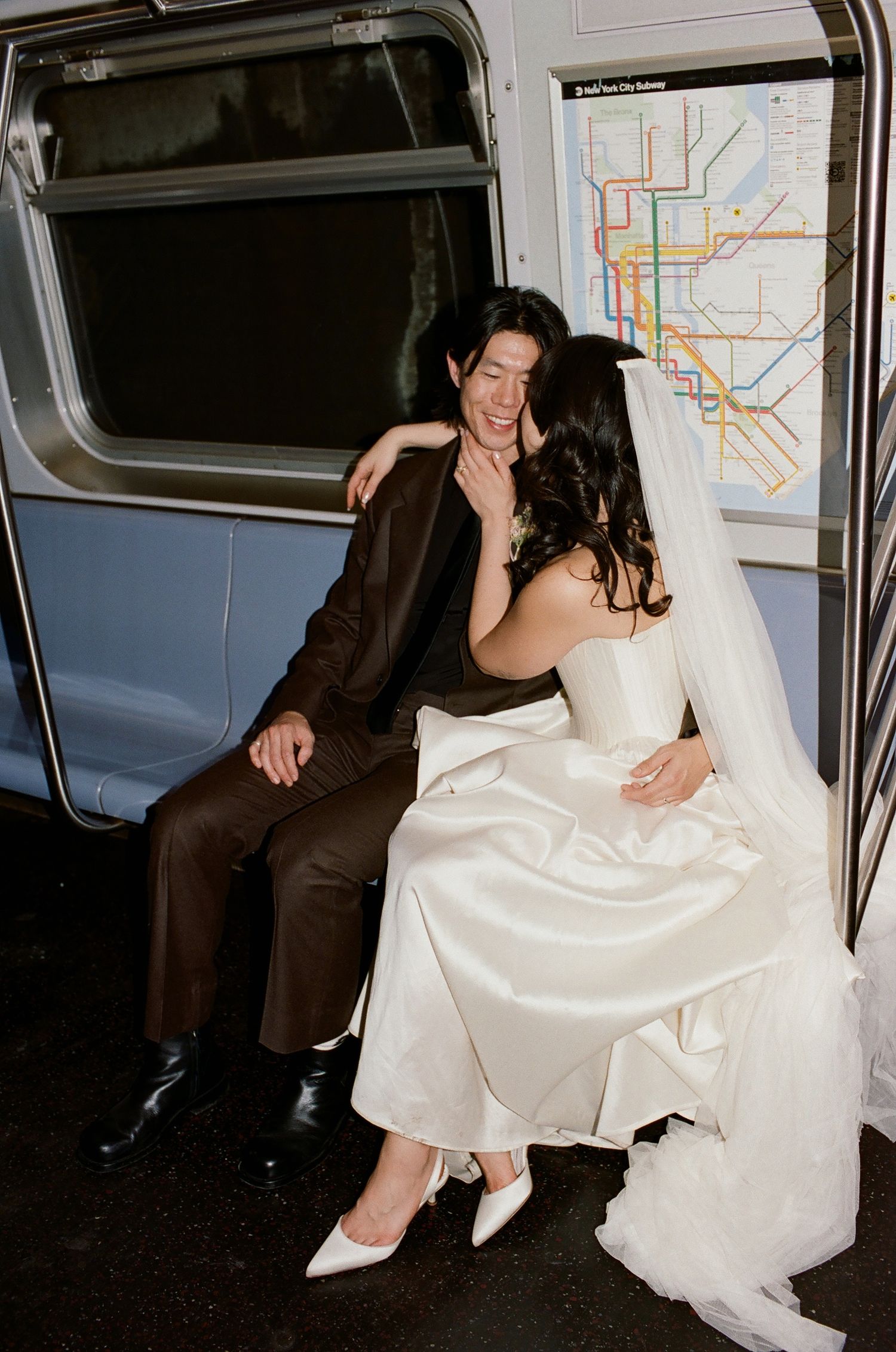 Newlywed couple in wedding attire sharing a romantic moment on a New York City subway car with transit map behind them.