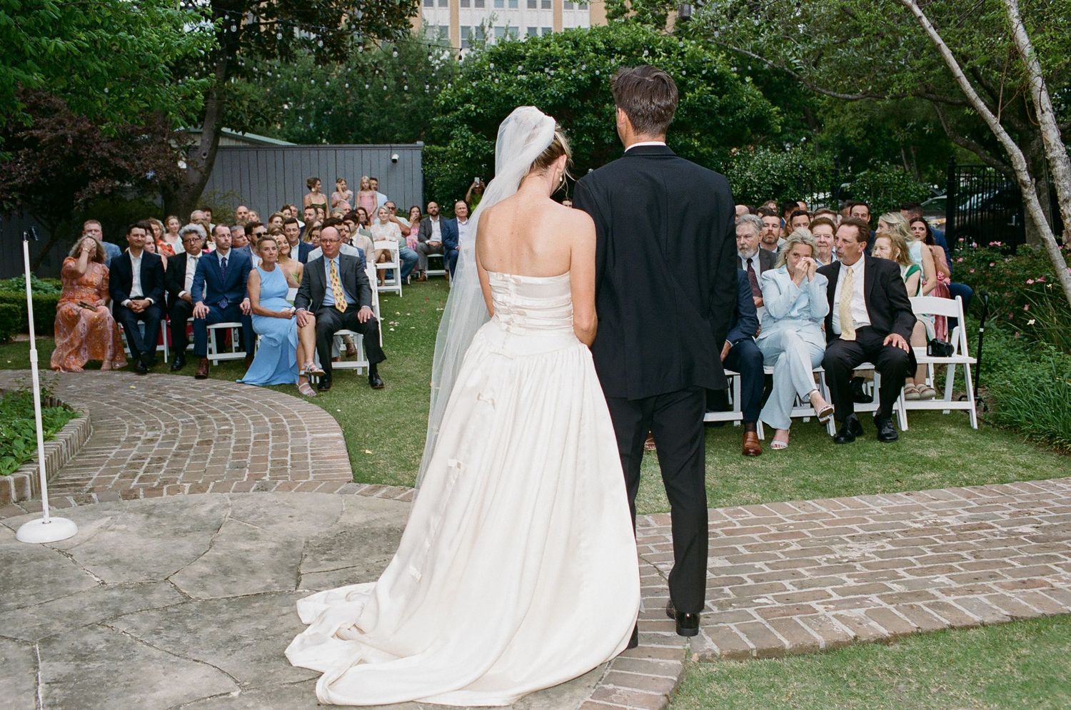 Newlyweds face officiant during outdoor ceremony with guests seated behind them.