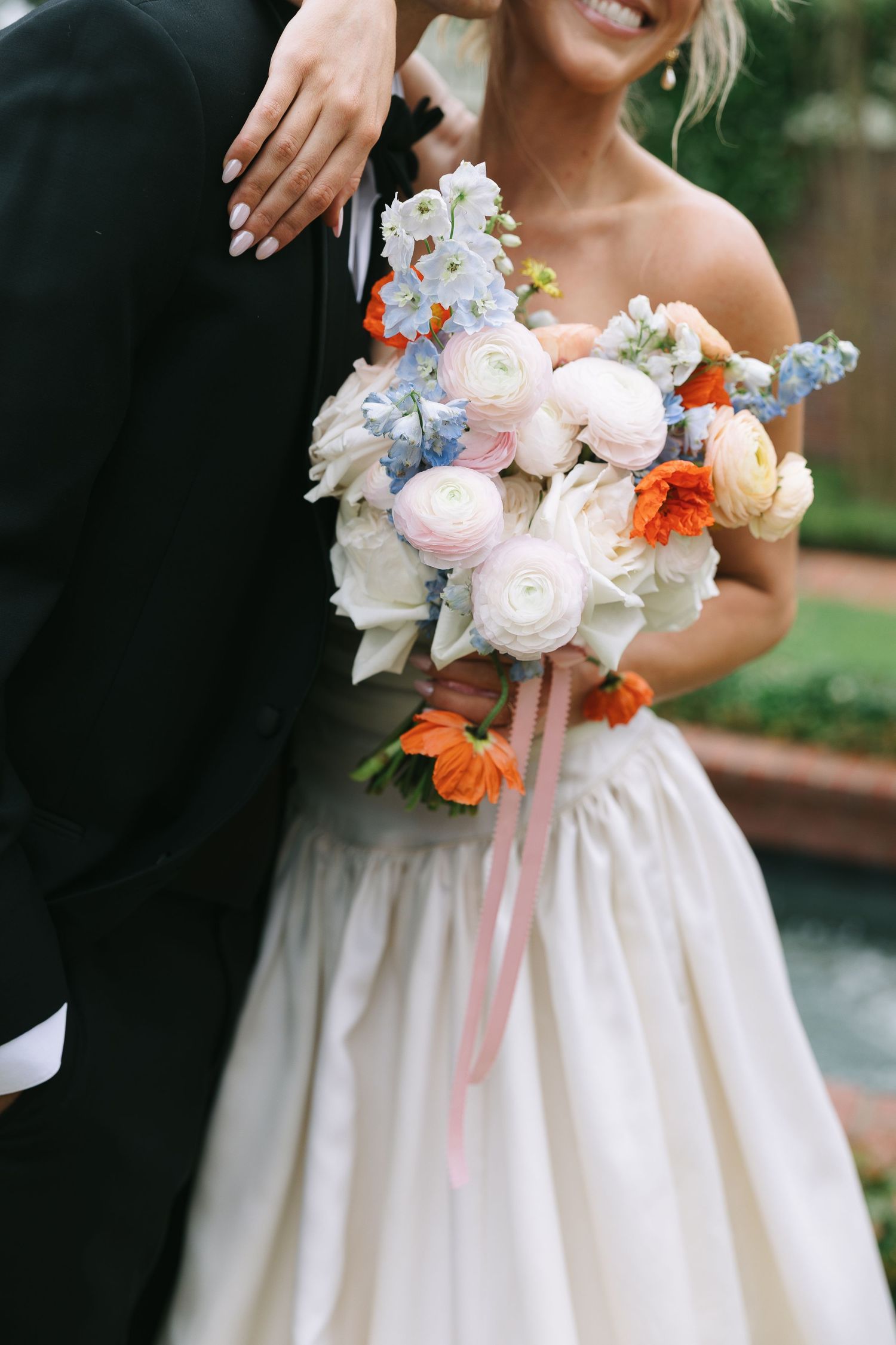Close-up of bridal bouquet featuring pink, orange, and blue flowers with flowing ribbons.