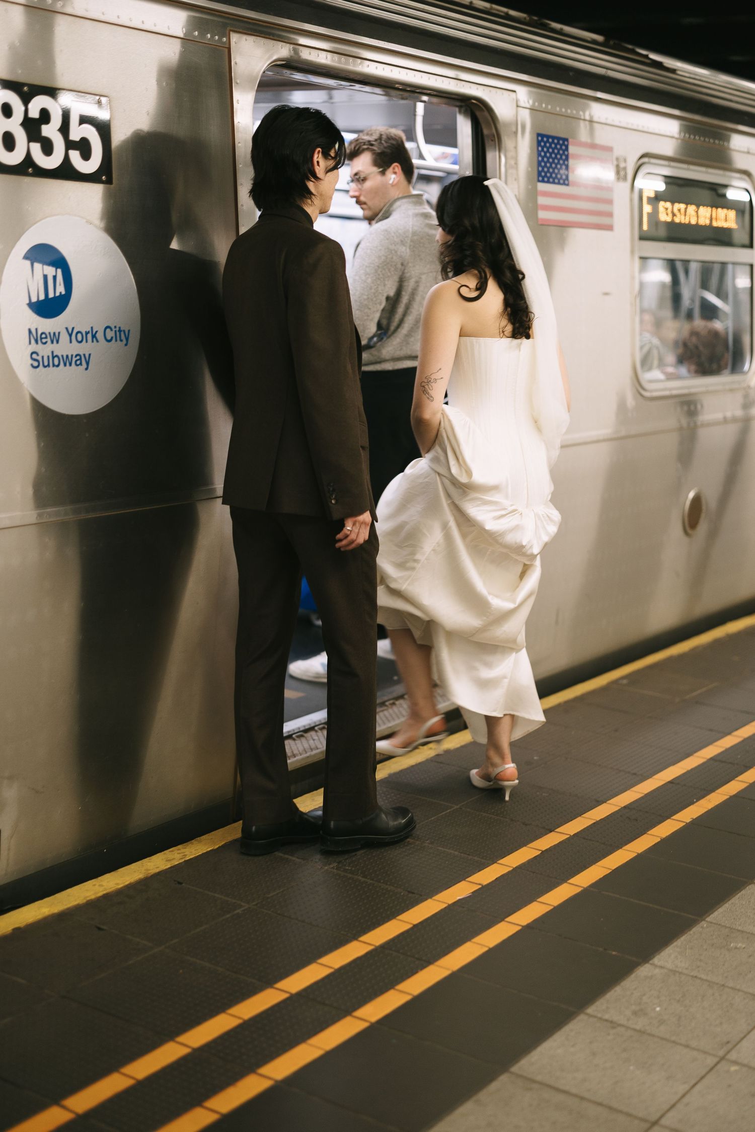 Wedding couple stands on New York City subway platform near train.