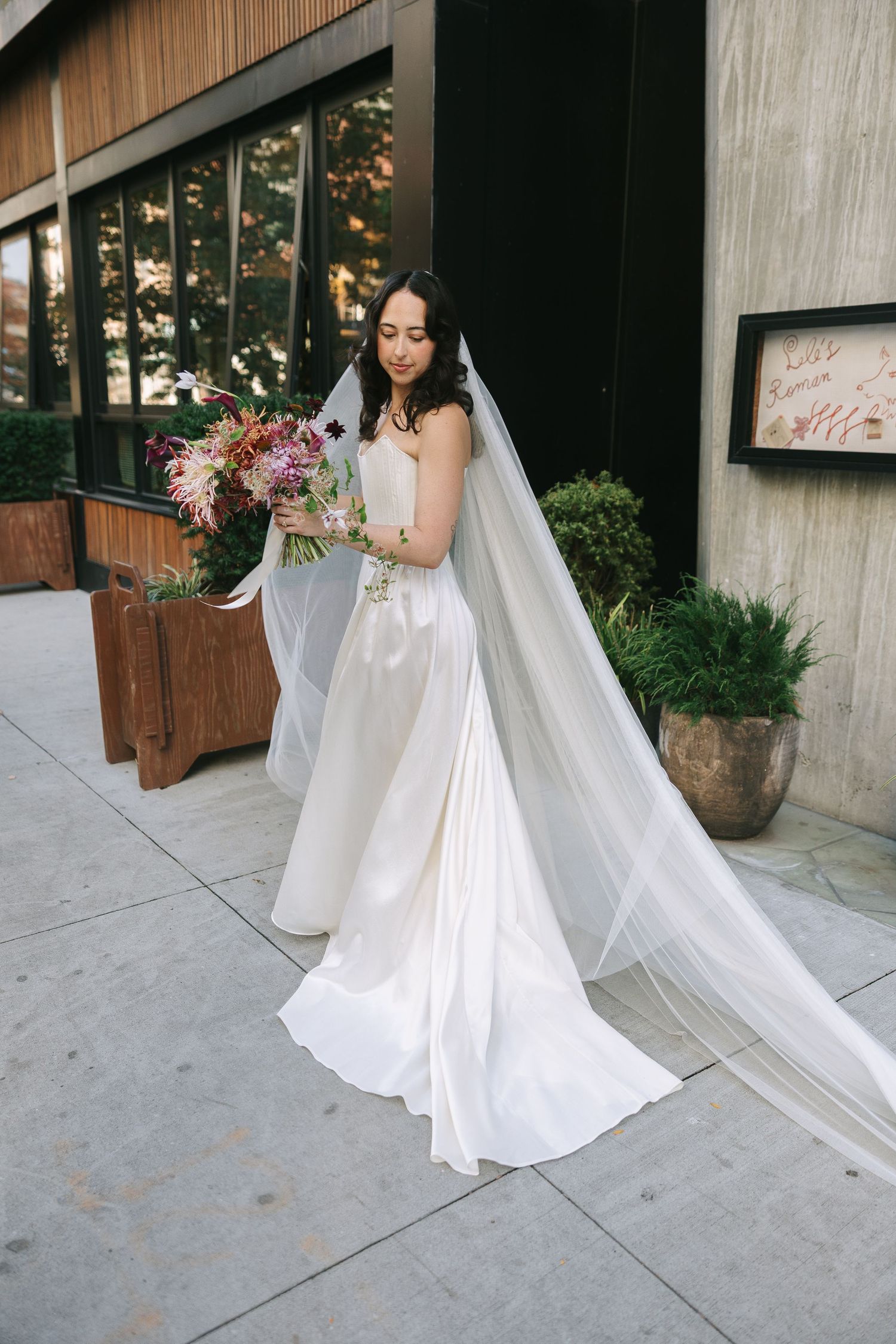 A bride holds a vibrant bouquet while posing in front of a modern building with wooden accents.