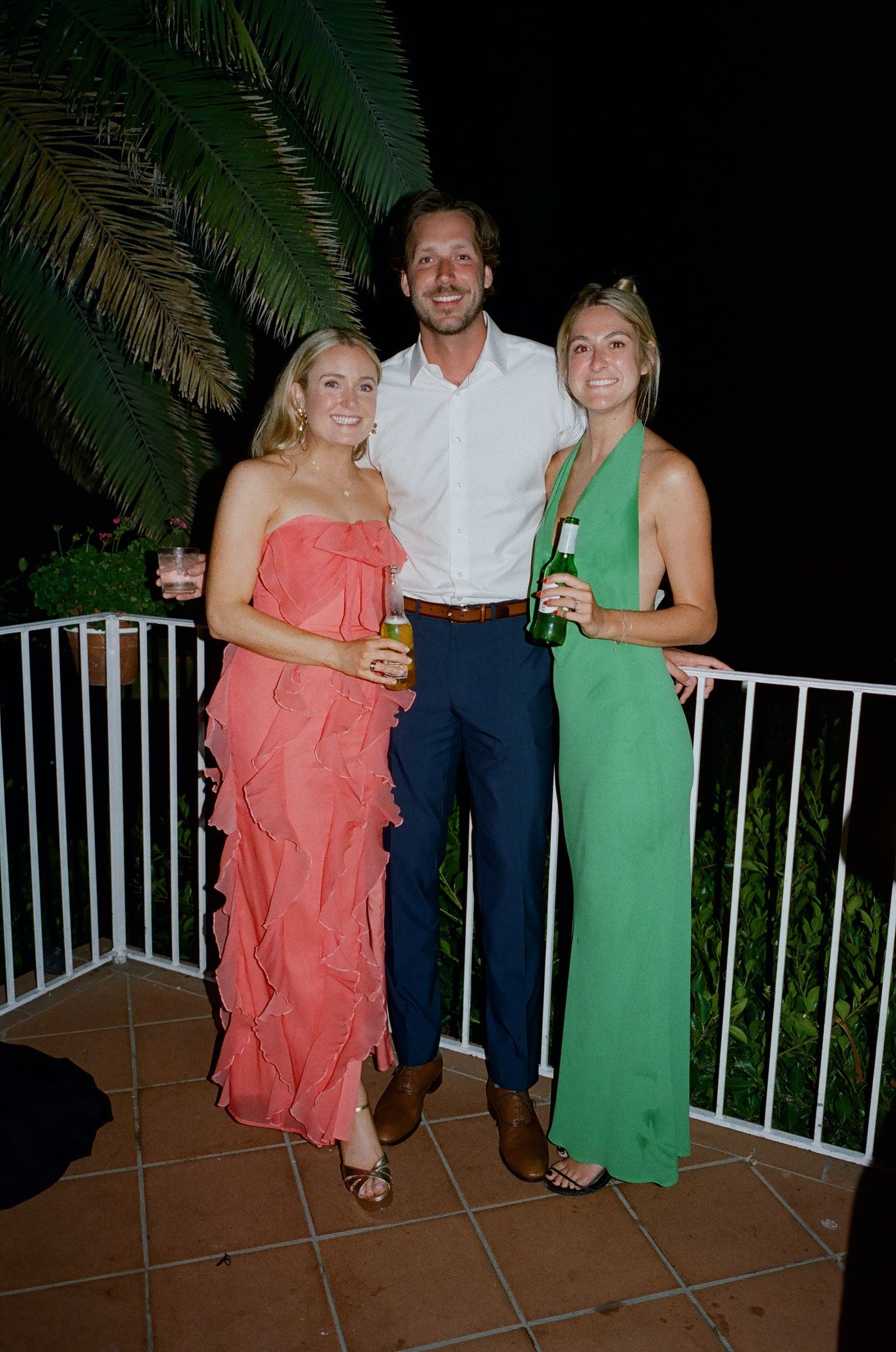 Three people in colorful summer attire pose on an outdoor patio at night.