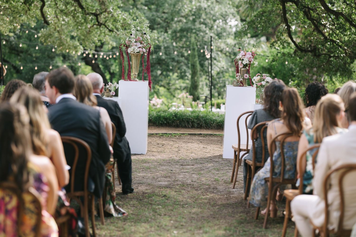 Guests seated in wooden chairs at an outdoor ceremony under tree canopy.