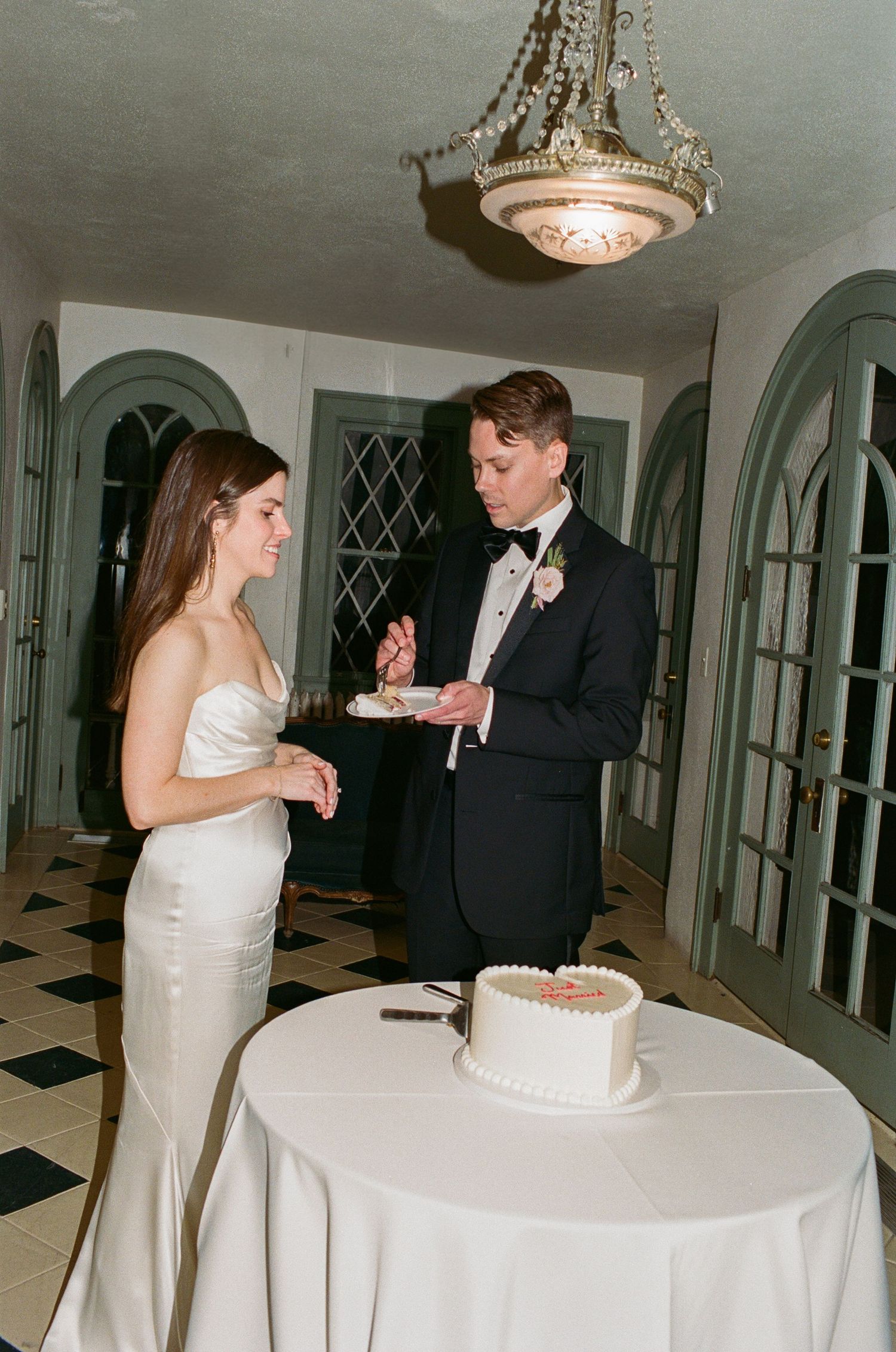 A couple sharing their first bite of wedding cake at an elegant indoor reception venue.
