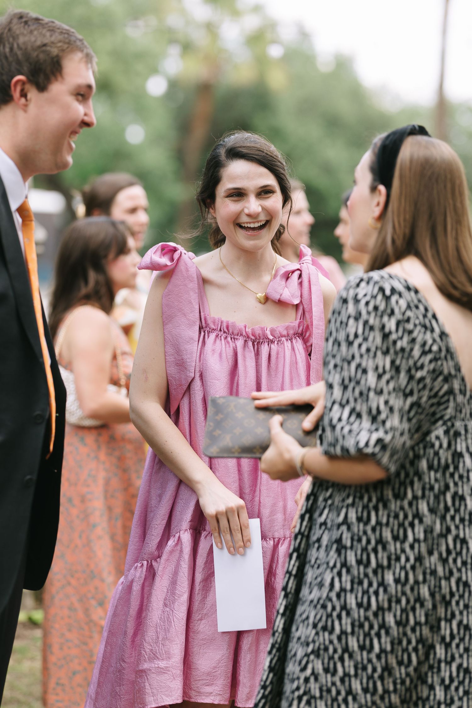 Wedding guests in colorful dresses mingle during an outdoor reception.