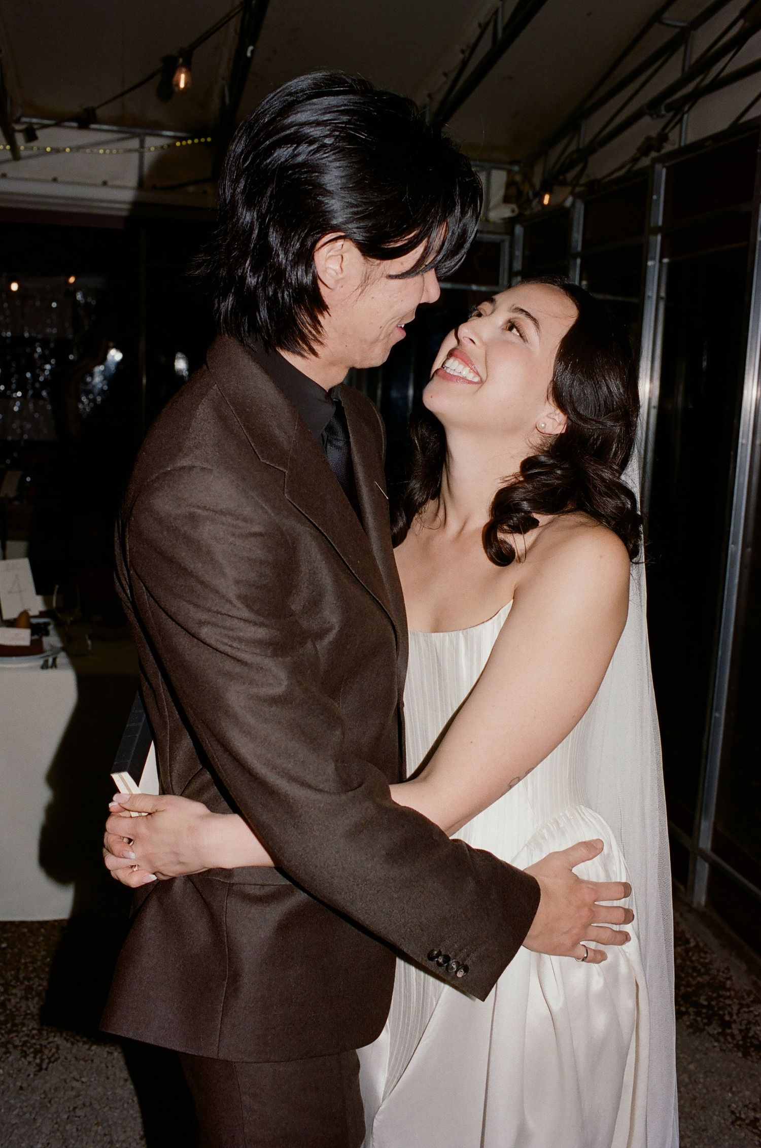 A couple in formal attire shares a romantic dance moment, with the woman in white and man in brown suit.
