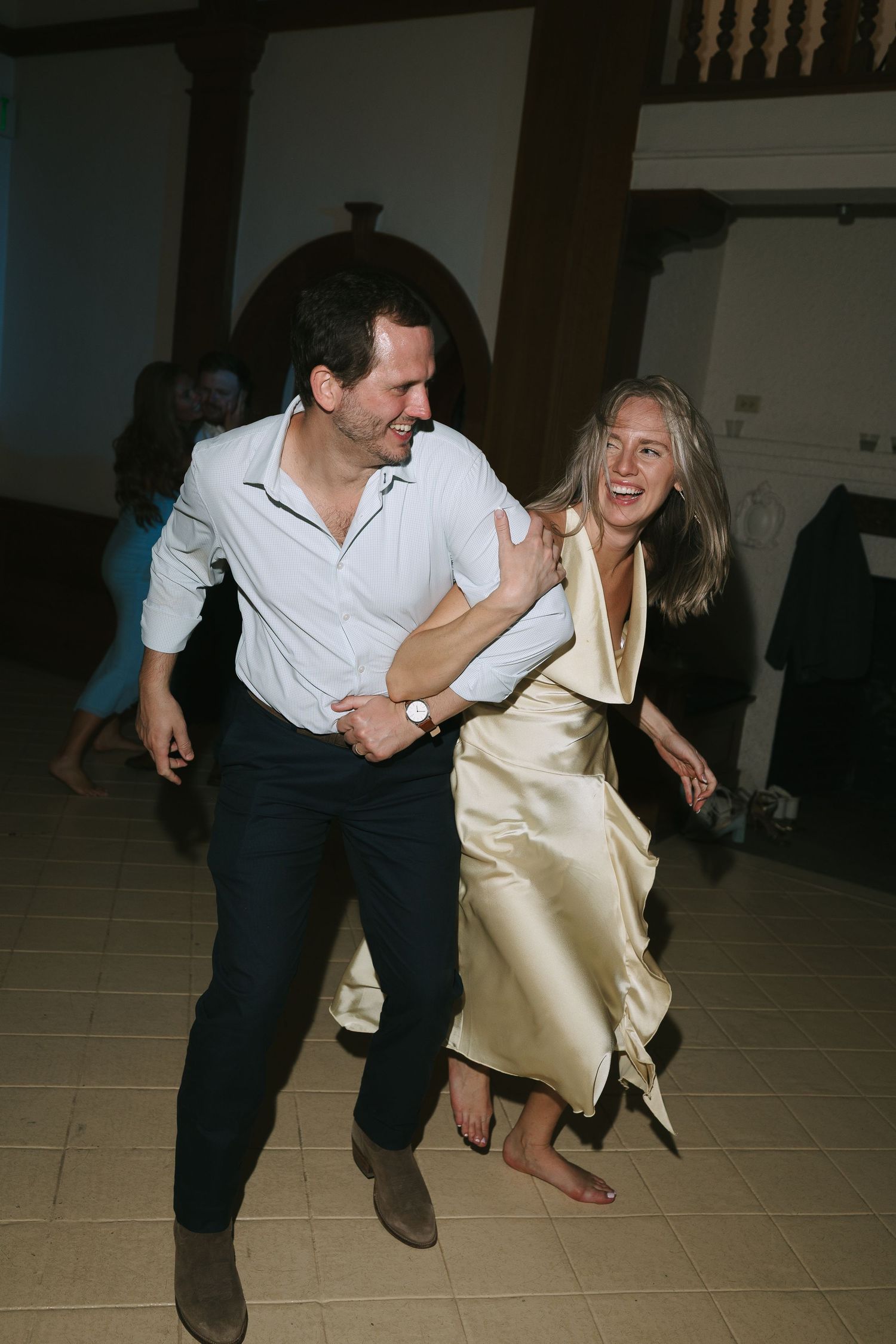 Couple dancing energetically on a tiled floor at a wedding reception.