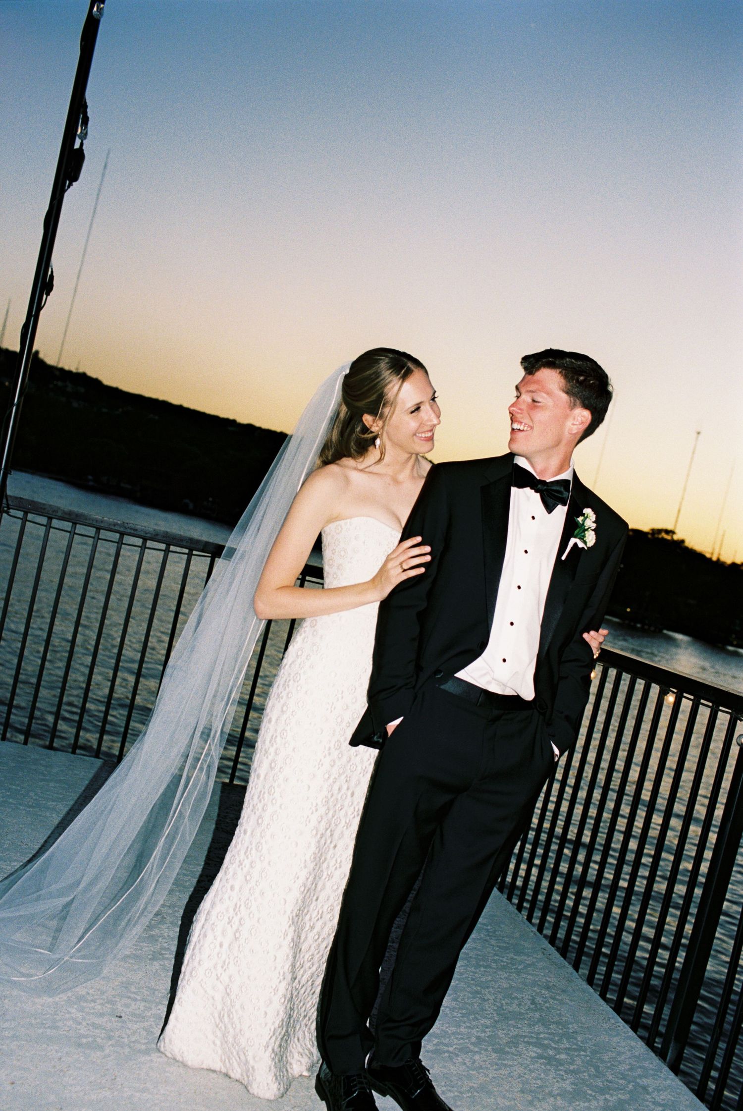 Sunset waterfront wedding portrait with couple against railing silhouette.