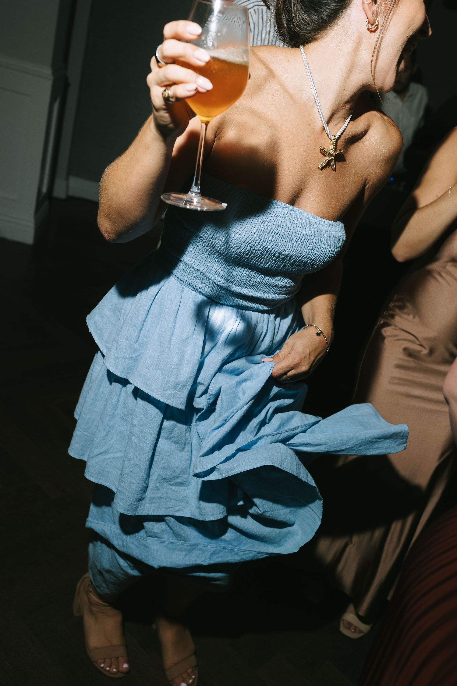 Person in a blue ruffled dress holding a wine glass at a dimly lit party.