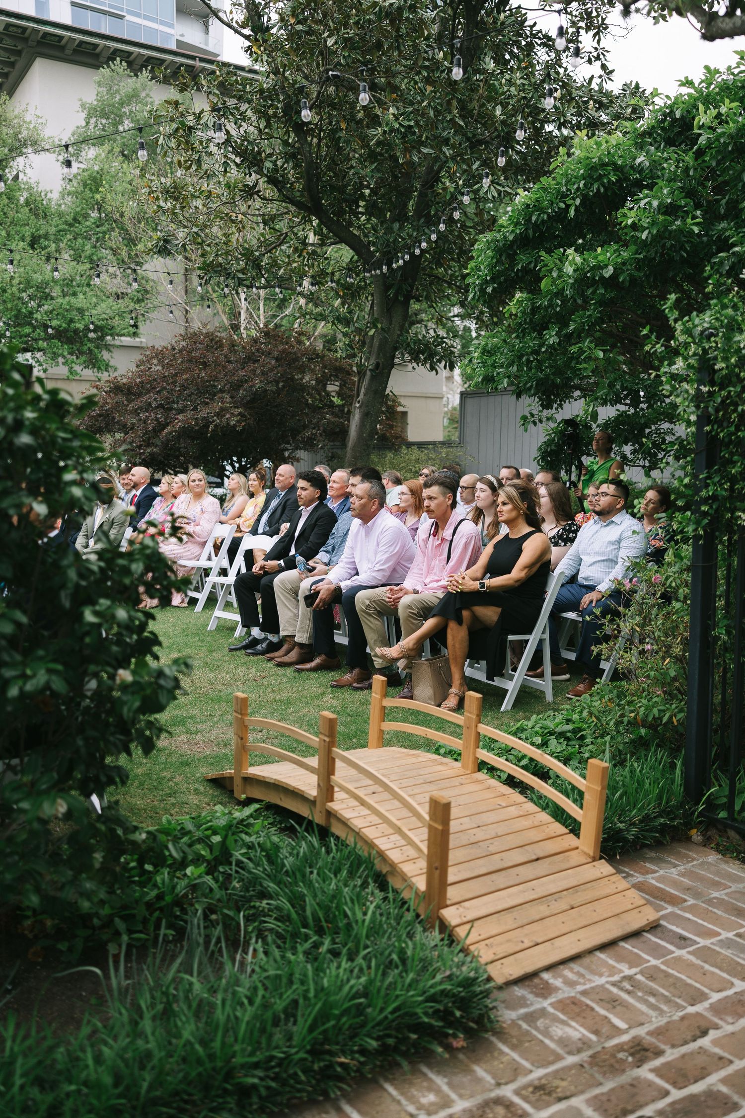 Wooden bridge with wedding guests seated in garden ceremony setting.