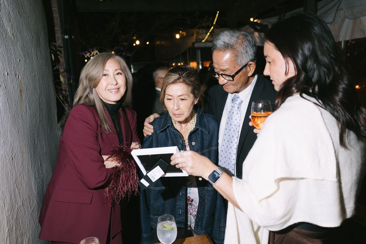 A group of people gather around to look at something on a digital device at a social gathering.