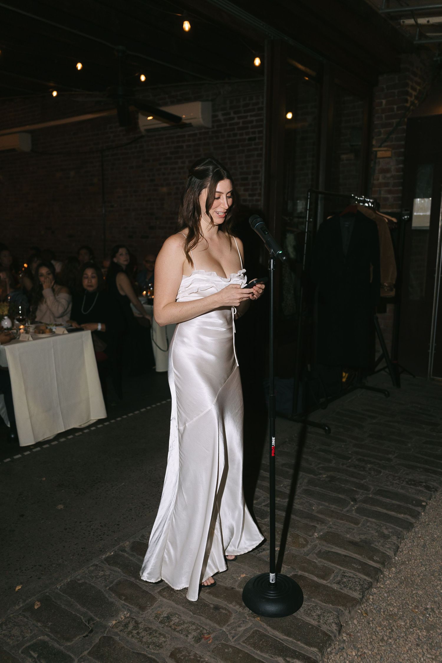 Person in white formal attire standing near tables at an indoor event space.