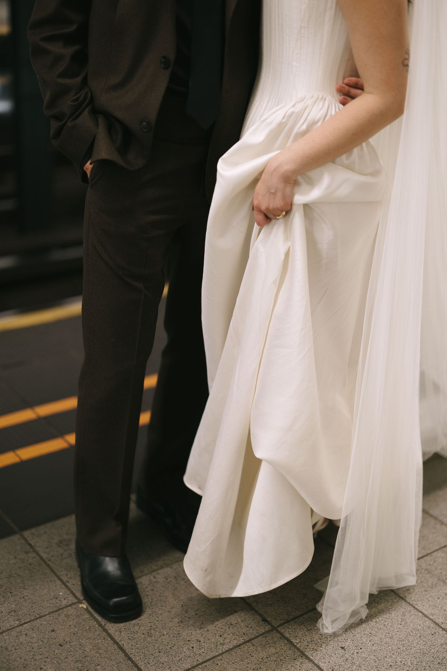 Wedding couple poses together showing details of white dress and dark suit.
