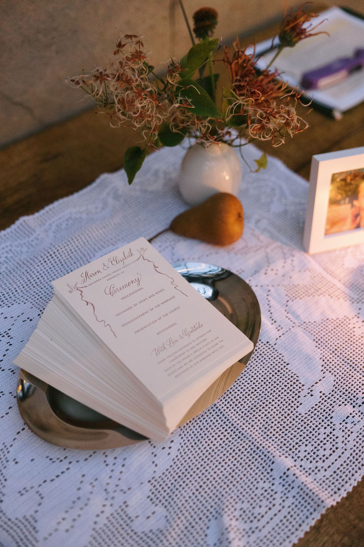 Wedding programs and details arranged on white lace tablecloth with floral accents.