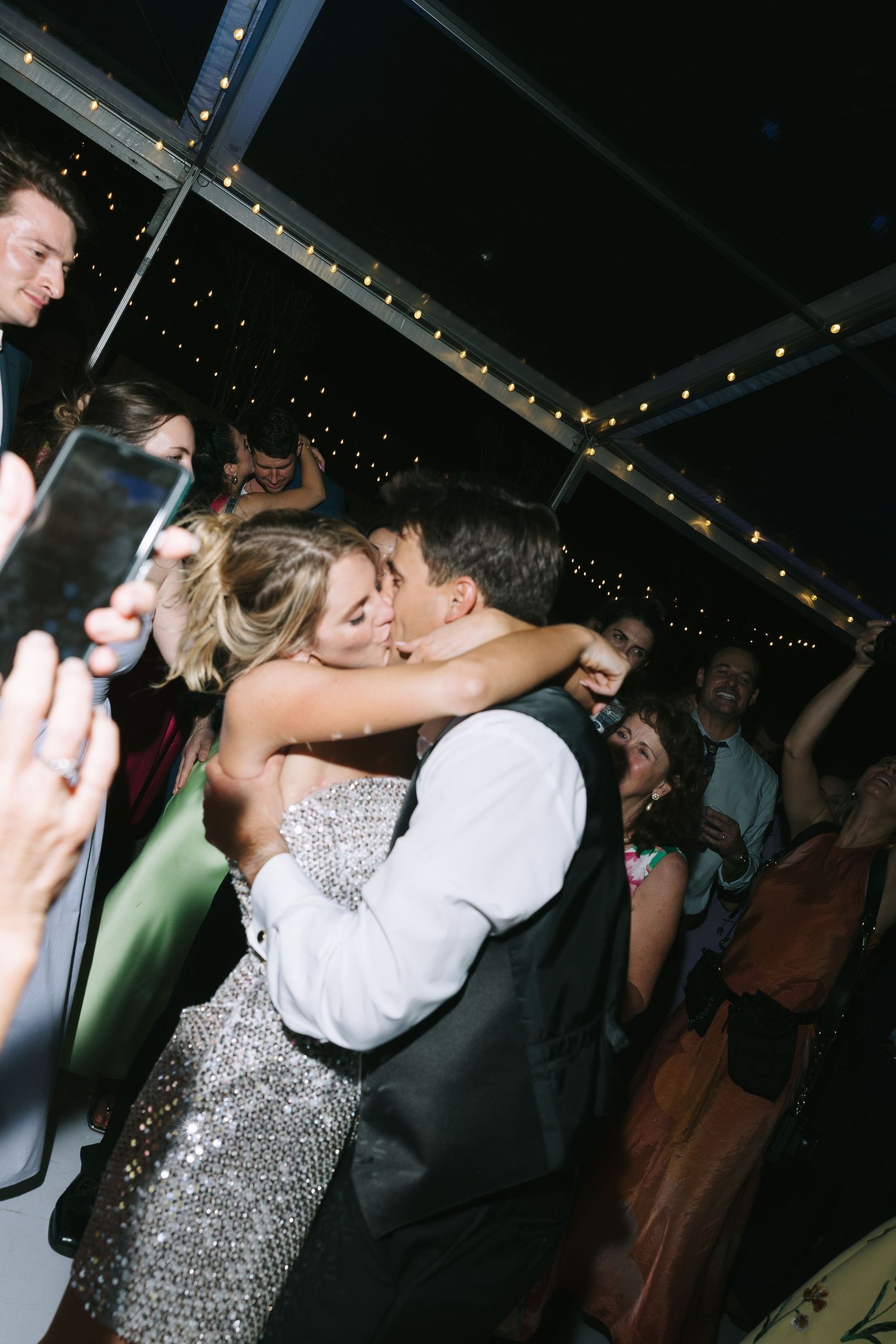A couple in formal attire share a romantic dance moment under twinkling lights at an evening reception.