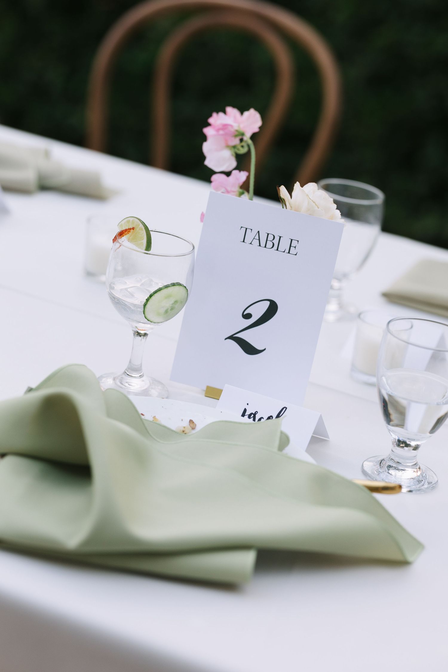 Table number cards and place settings with soft green napkins at an elegant reception.