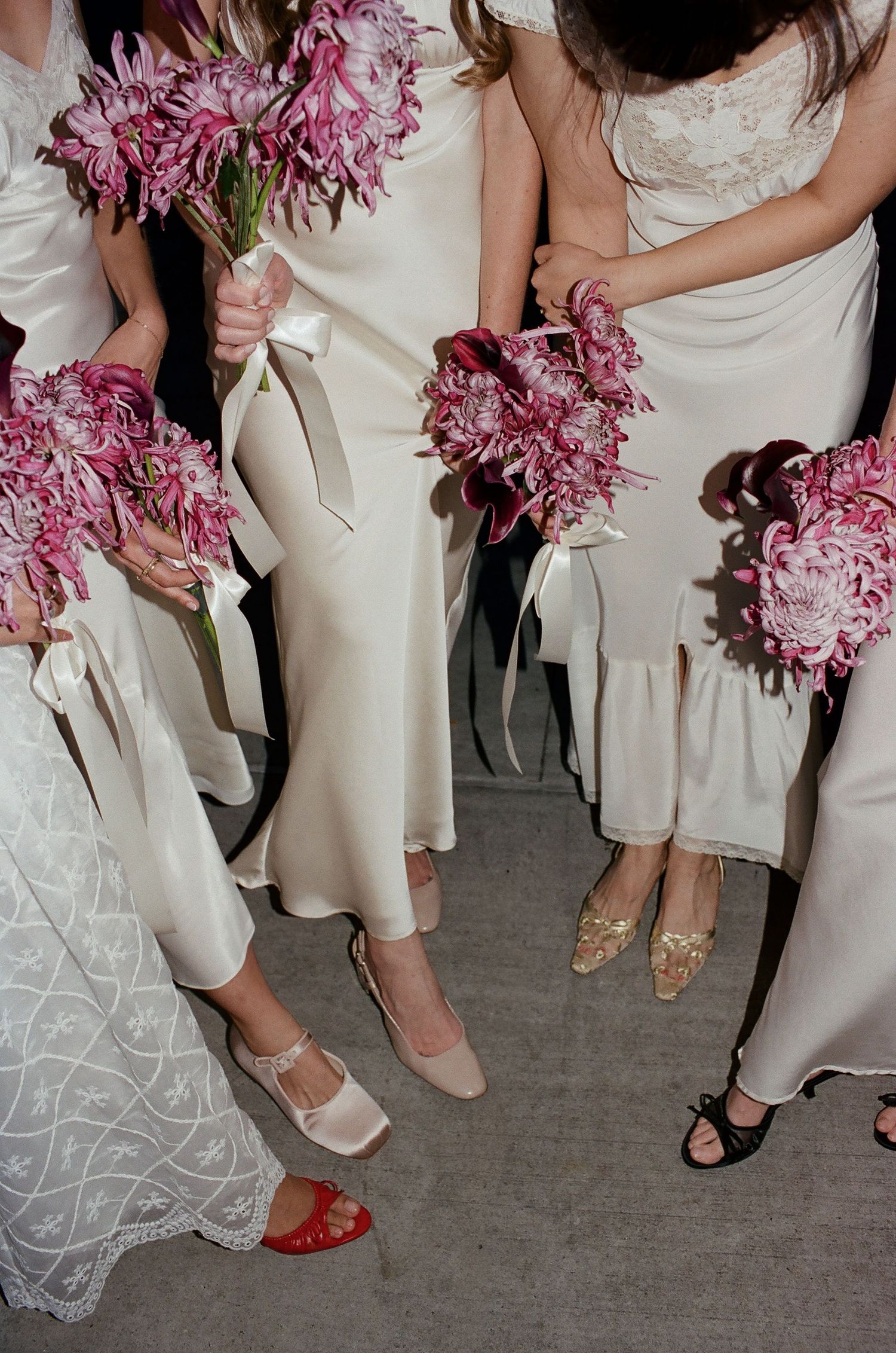 A row of bridesmaids in cream dresses holding pink bouquets with their shoes visible at the bottom of the frame.