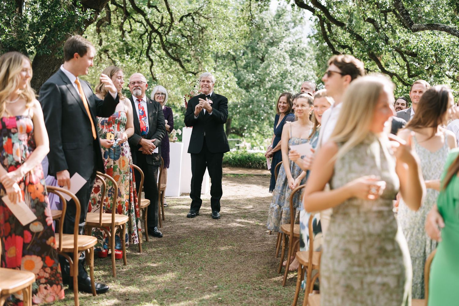 Wedding guests seated in wooden chairs during an outdoor garden ceremony.