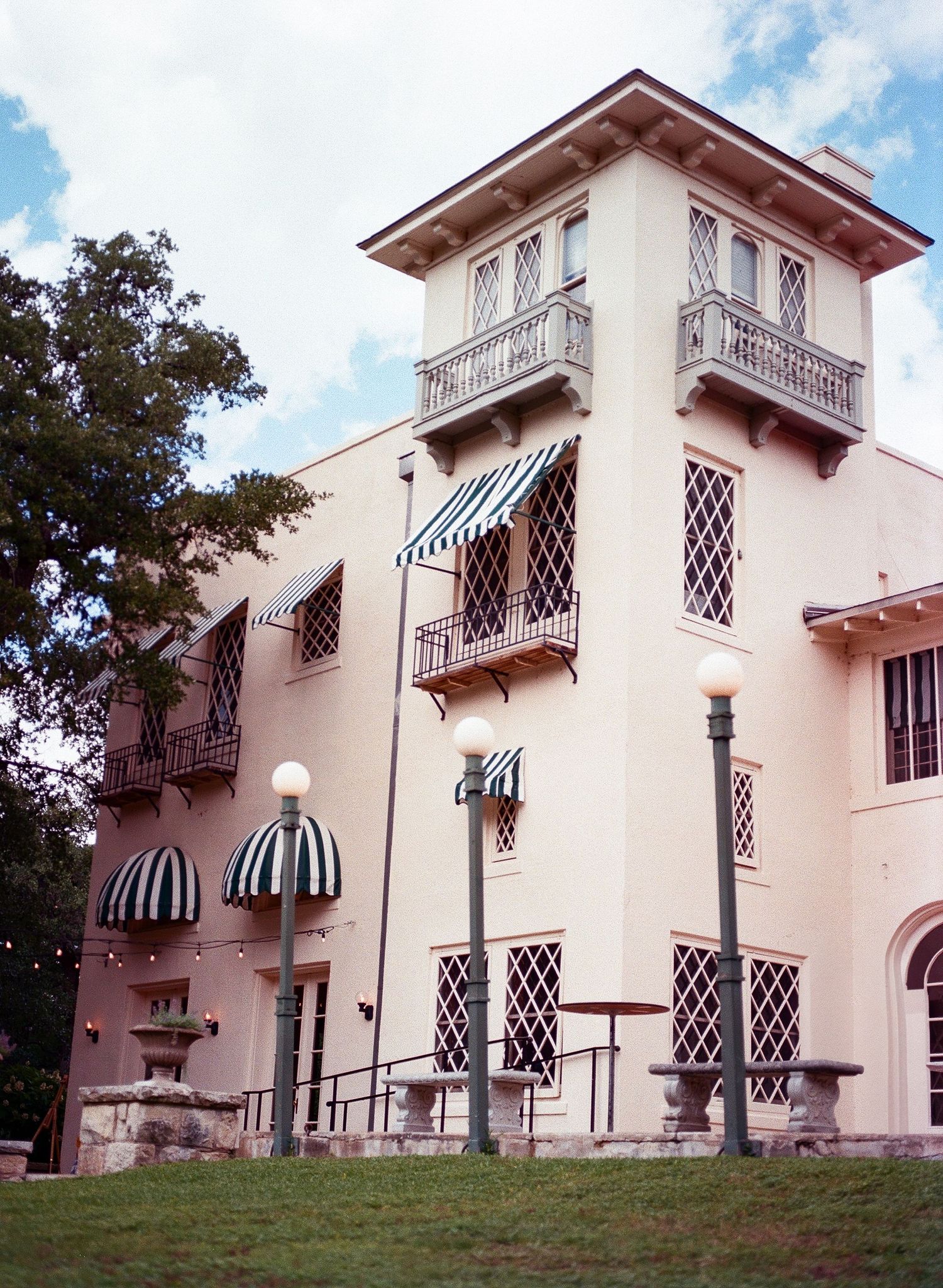 Elegant Mediterranean-style villa with white walls and striped awnings viewed from the lawn.