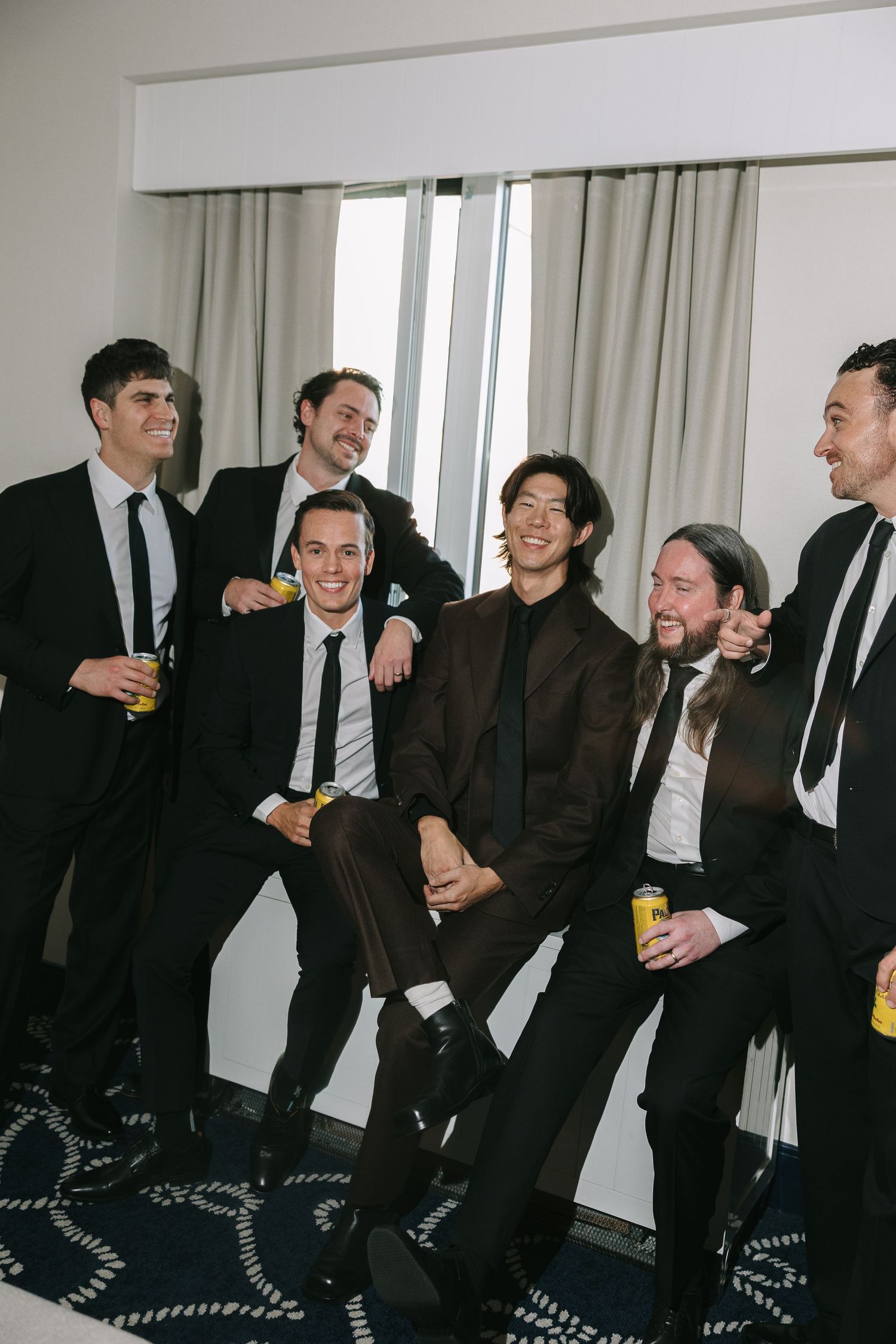 Group of men in suits laughing and socializing at an indoor gathering.