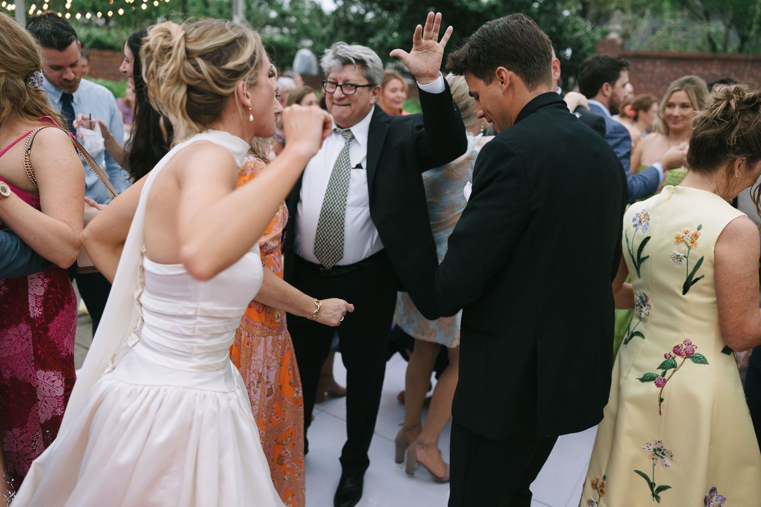 Wedding party members dance in a circle at an outdoor celebration.