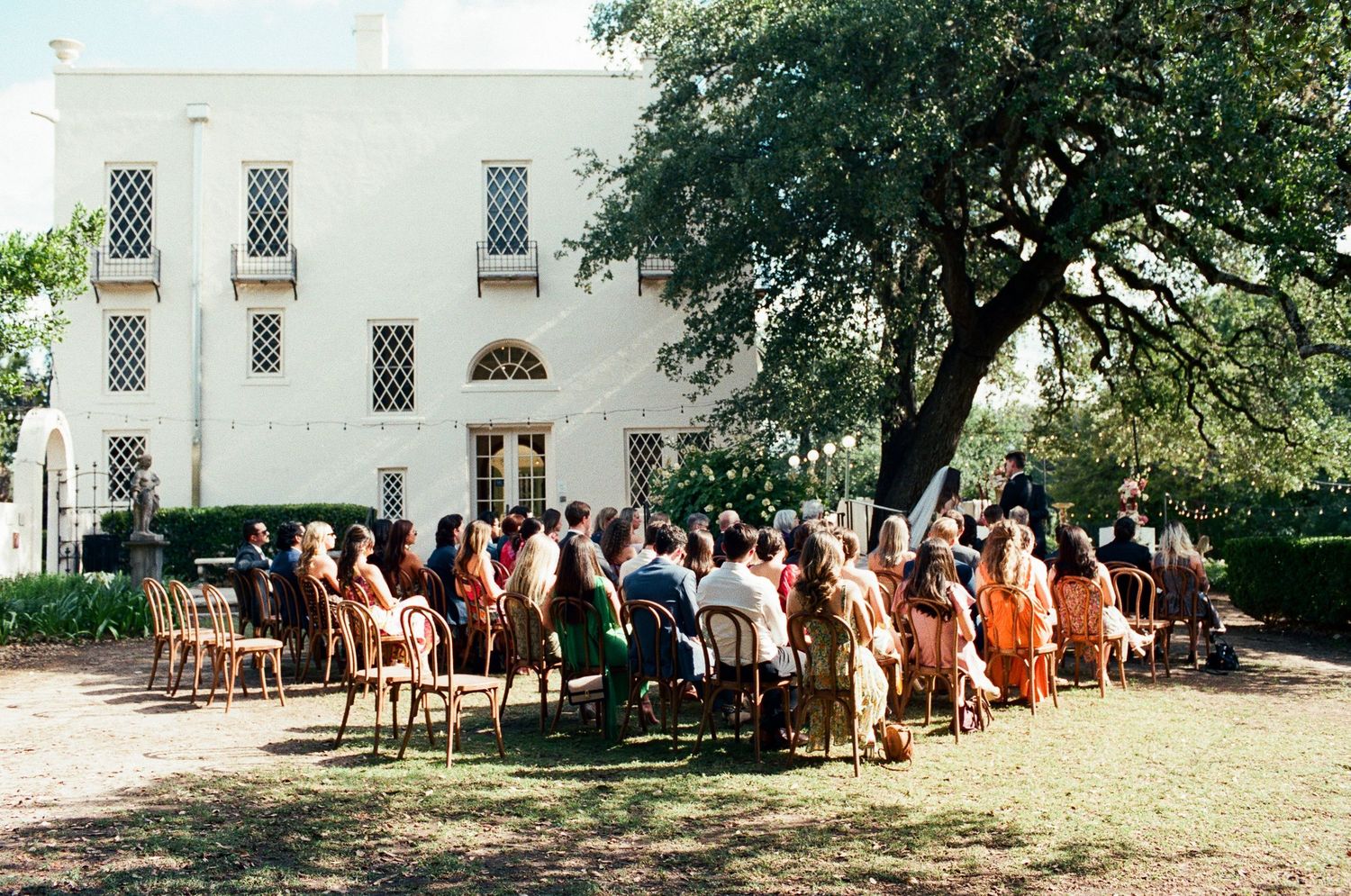 Outdoor wedding ceremony setup with wooden chairs facing a white building.