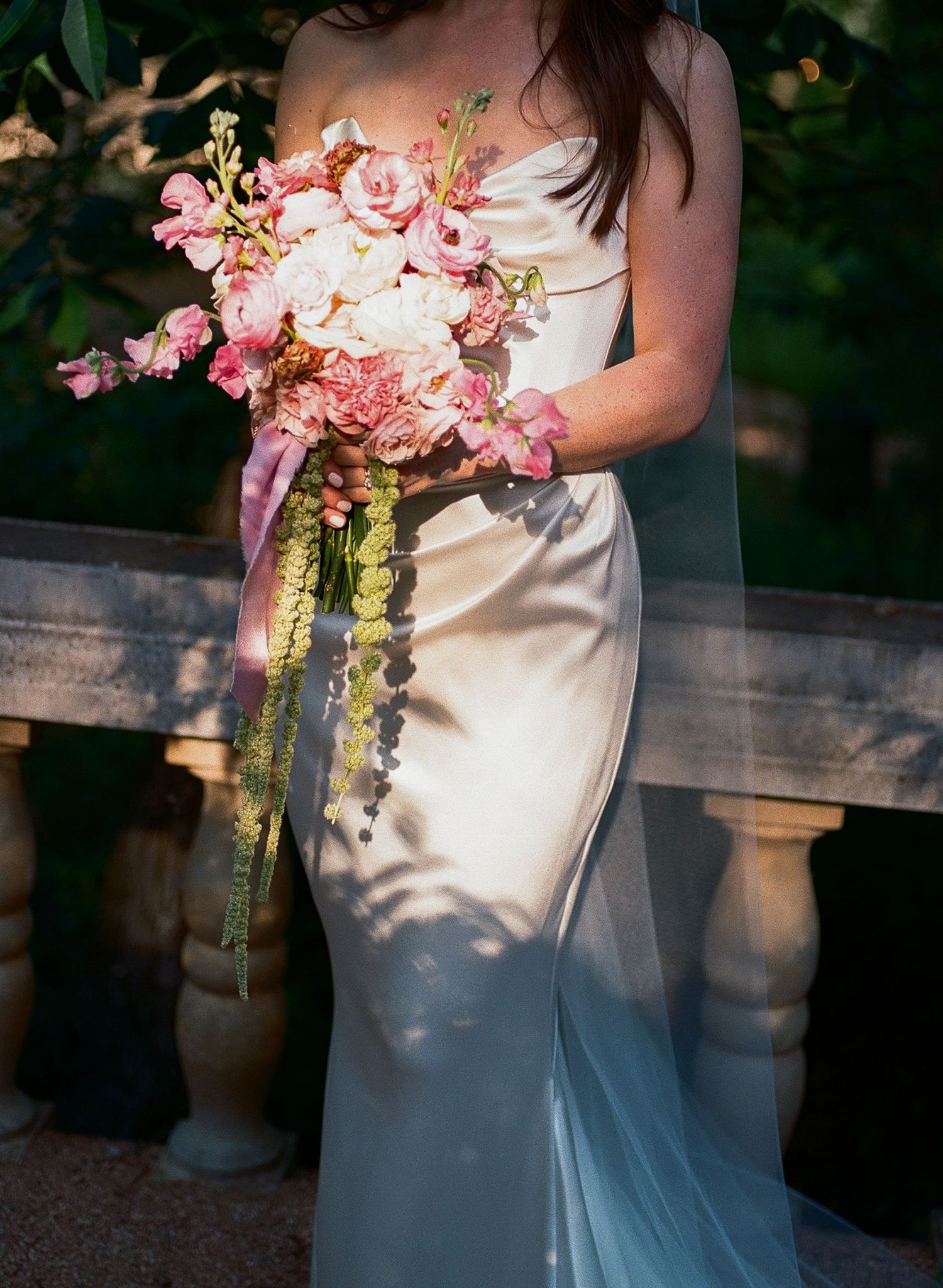 Detail shot of a pink bridal bouquet with cascading ribbons against a white wedding dress.