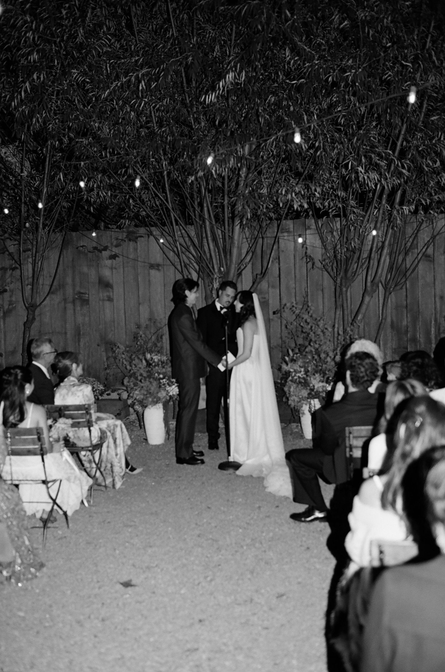 A black and white photograph shows people gathered outdoors at night for what appears to be a formal event.