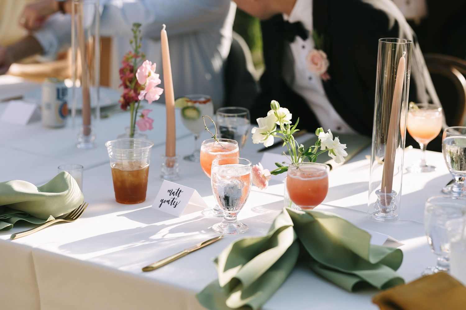 Elegant table settings with water glasses and pink drinks at outdoor reception.
