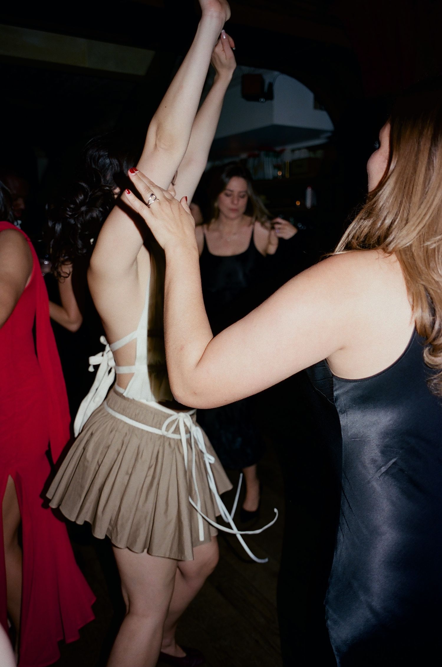 Women dancing together at a party, wearing stylish dresses in a dimly lit venue.