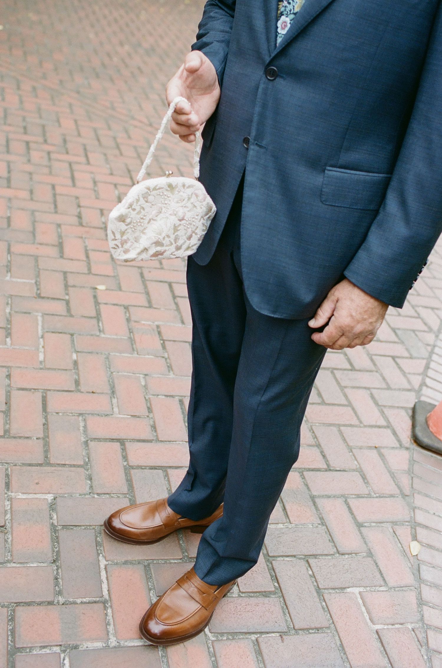 Detail shot of groom's navy suit and brown leather shoes on brick pavement.