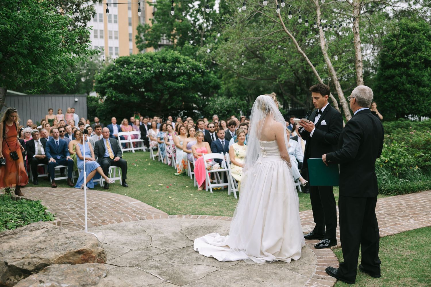 Outdoor wedding ceremony setup with brick pathway and natural greenery surroundings.