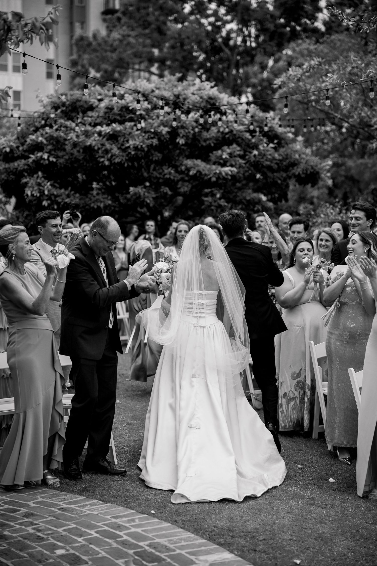 Wedding guests in formal attire standing and taking photos during outdoor ceremony.