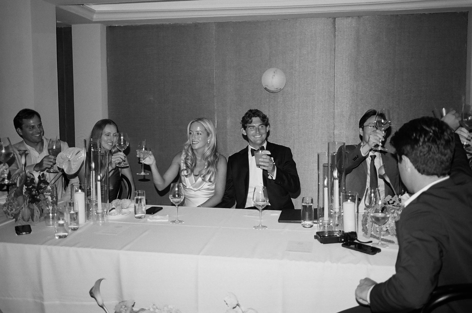 Wedding reception guests seated at a formal dinner table with candles and glassware.