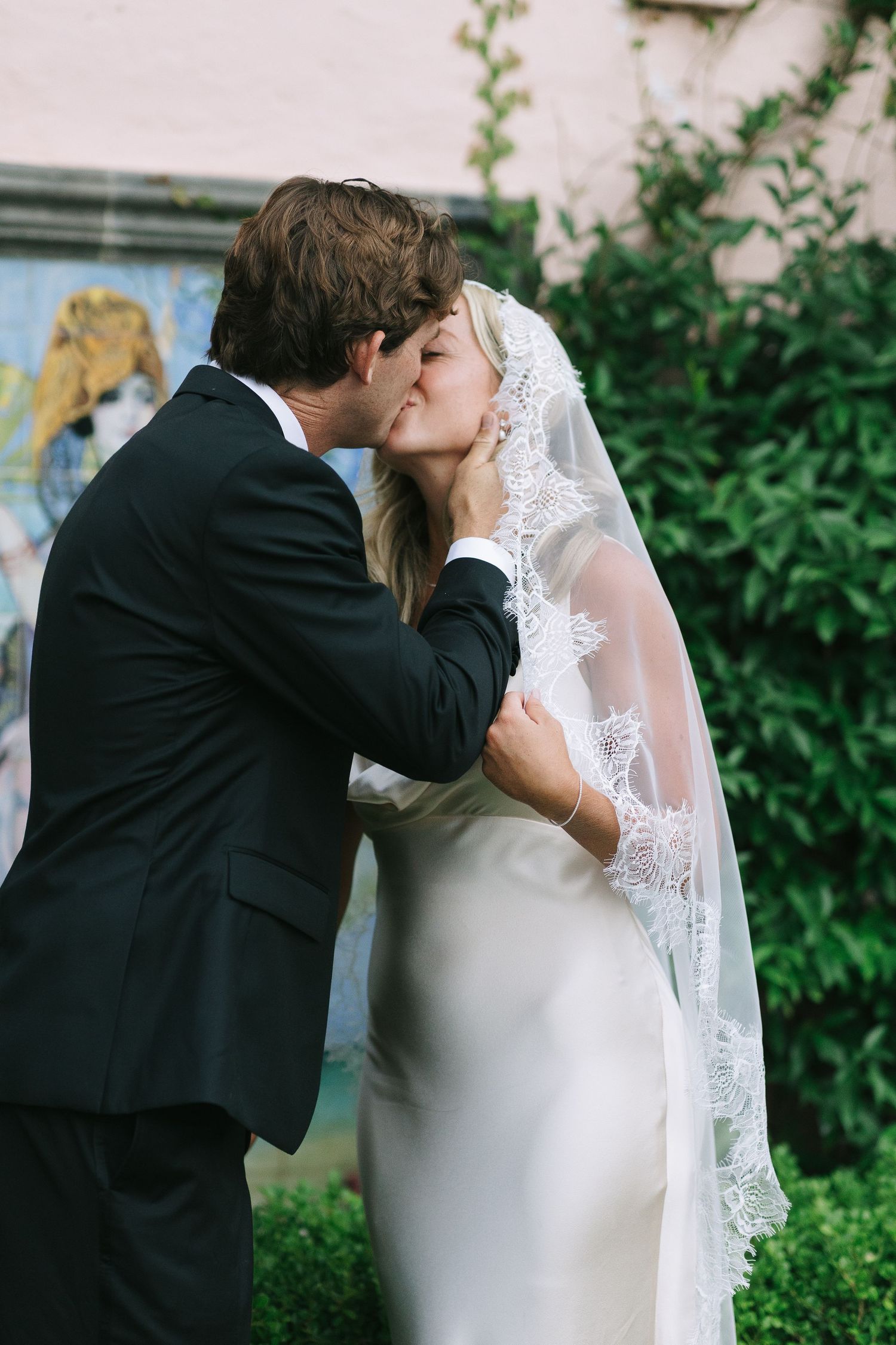 A romantic wedding moment captured in a garden setting with a couple sharing their first kiss.