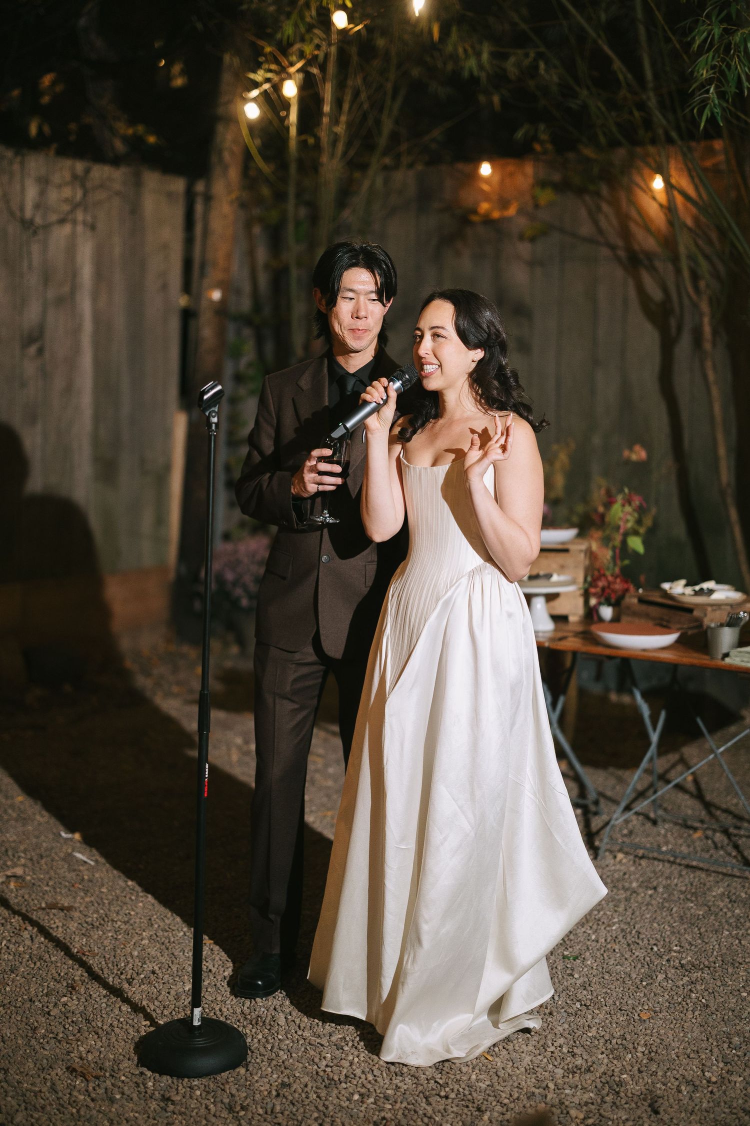 A couple performs together with microphones at their outdoor wedding reception.