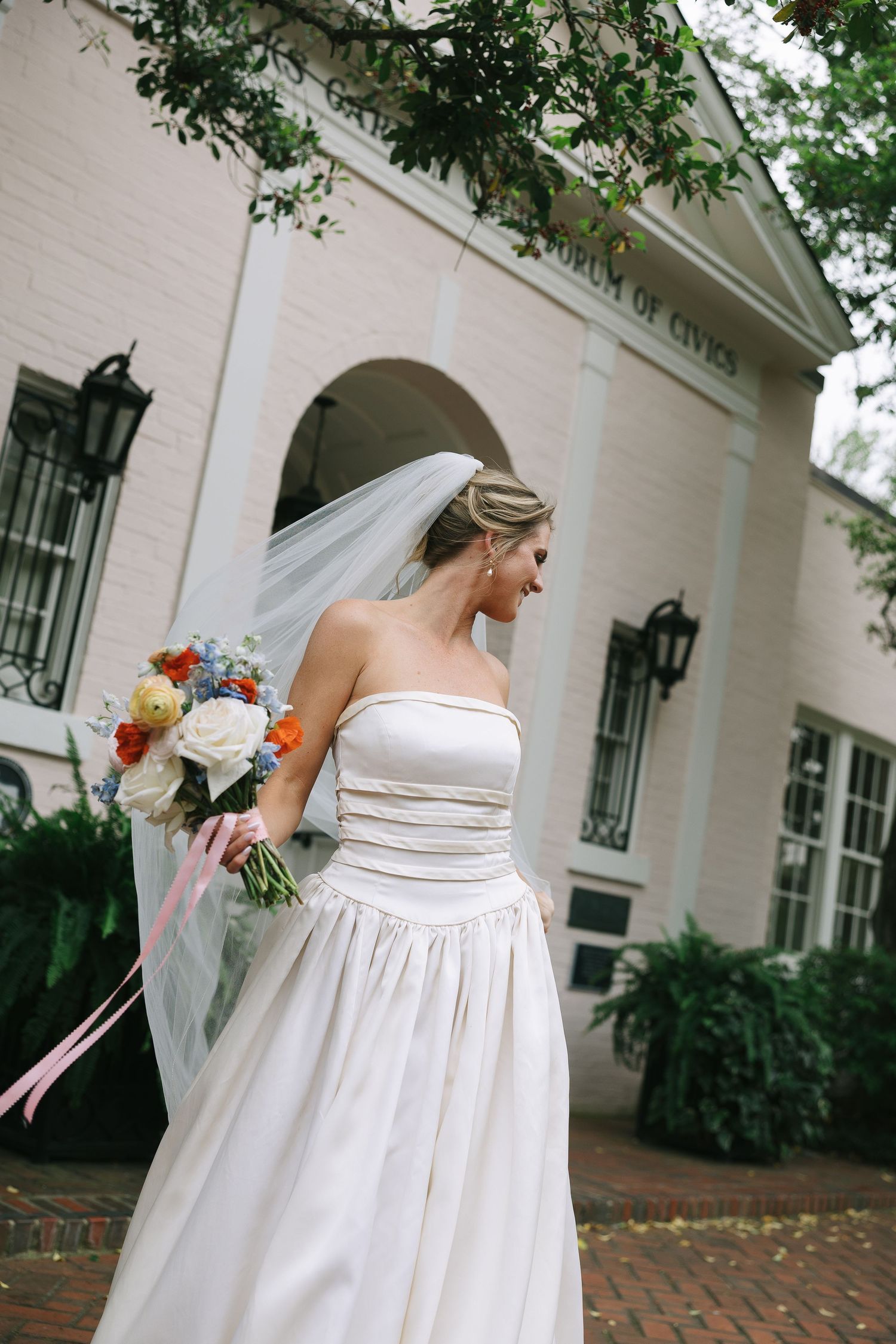 Candid moments of a bride in her elegant white dress outside a colonial-style building.