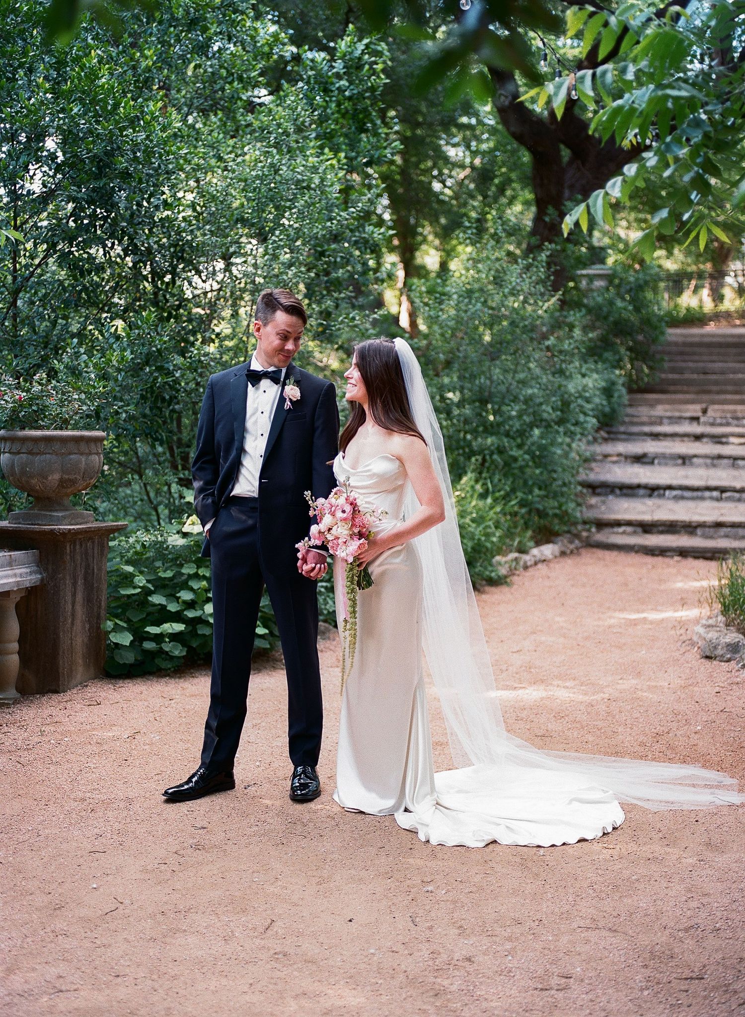 Newlyweds sharing intimate moments in a garden setting with stone steps.