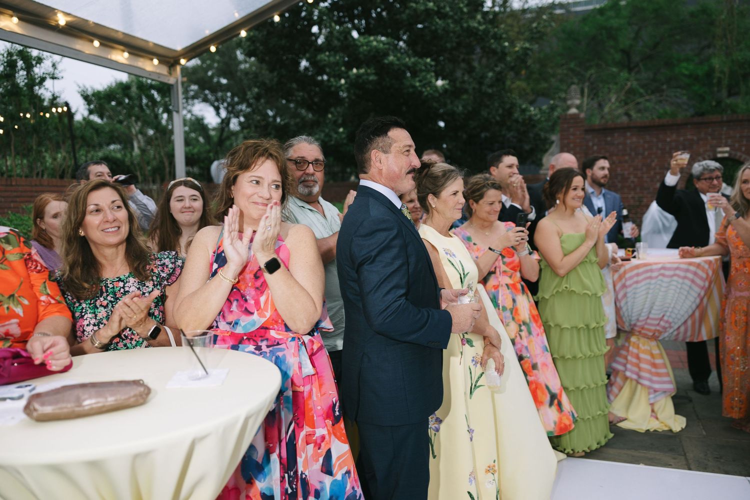 Wedding guests in colorful attire gather at an outdoor reception under a tent.