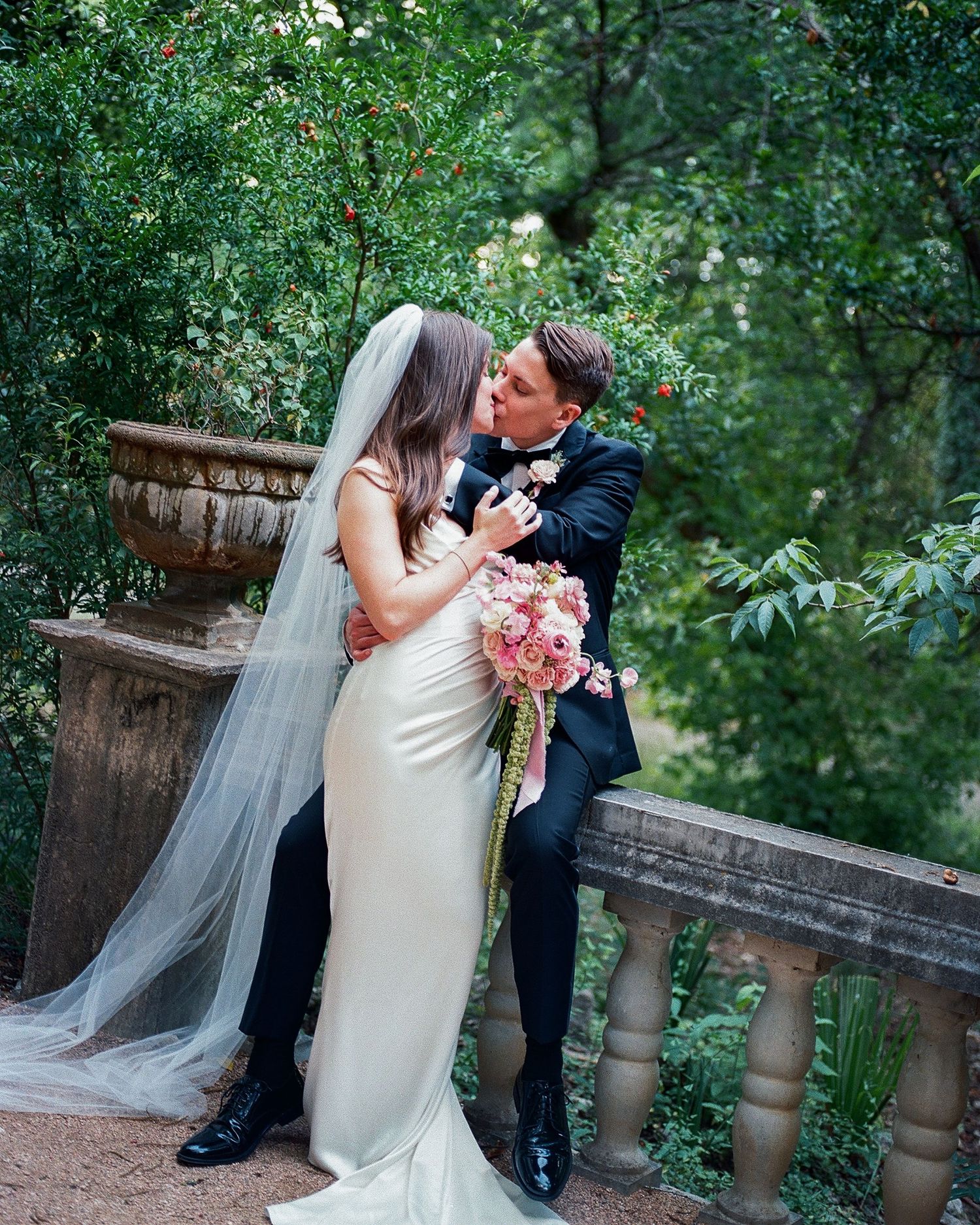 Romantic wedding couple posing in a lush garden setting with stone balustrade.