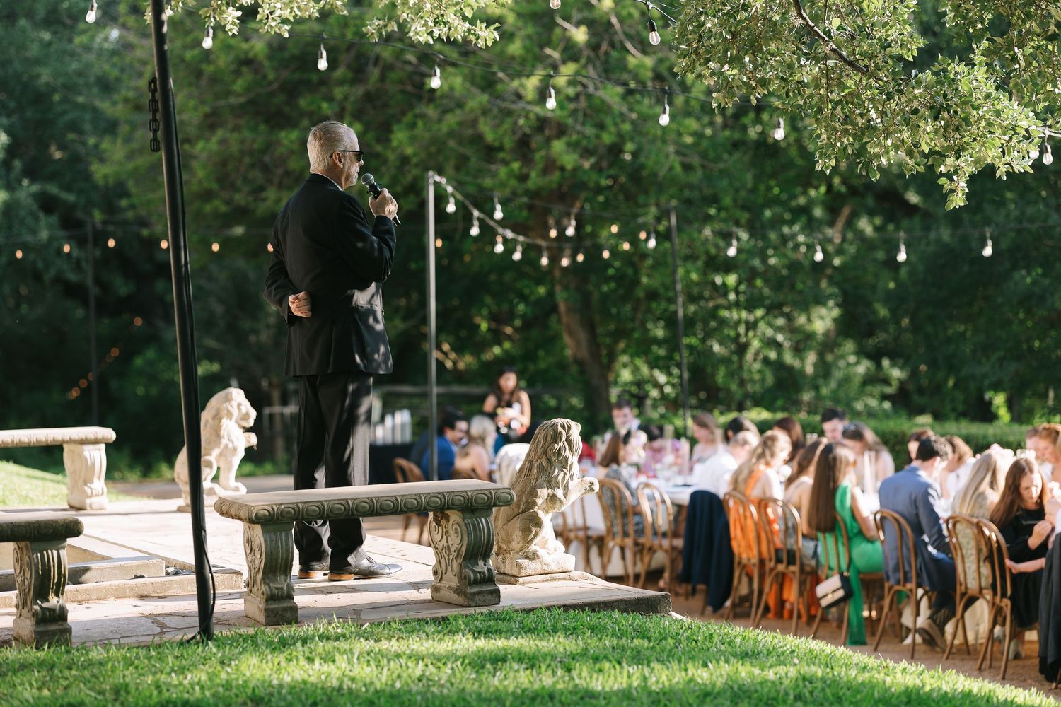 Elegant outdoor wedding reception setup with wooden chairs and string lights under trees.