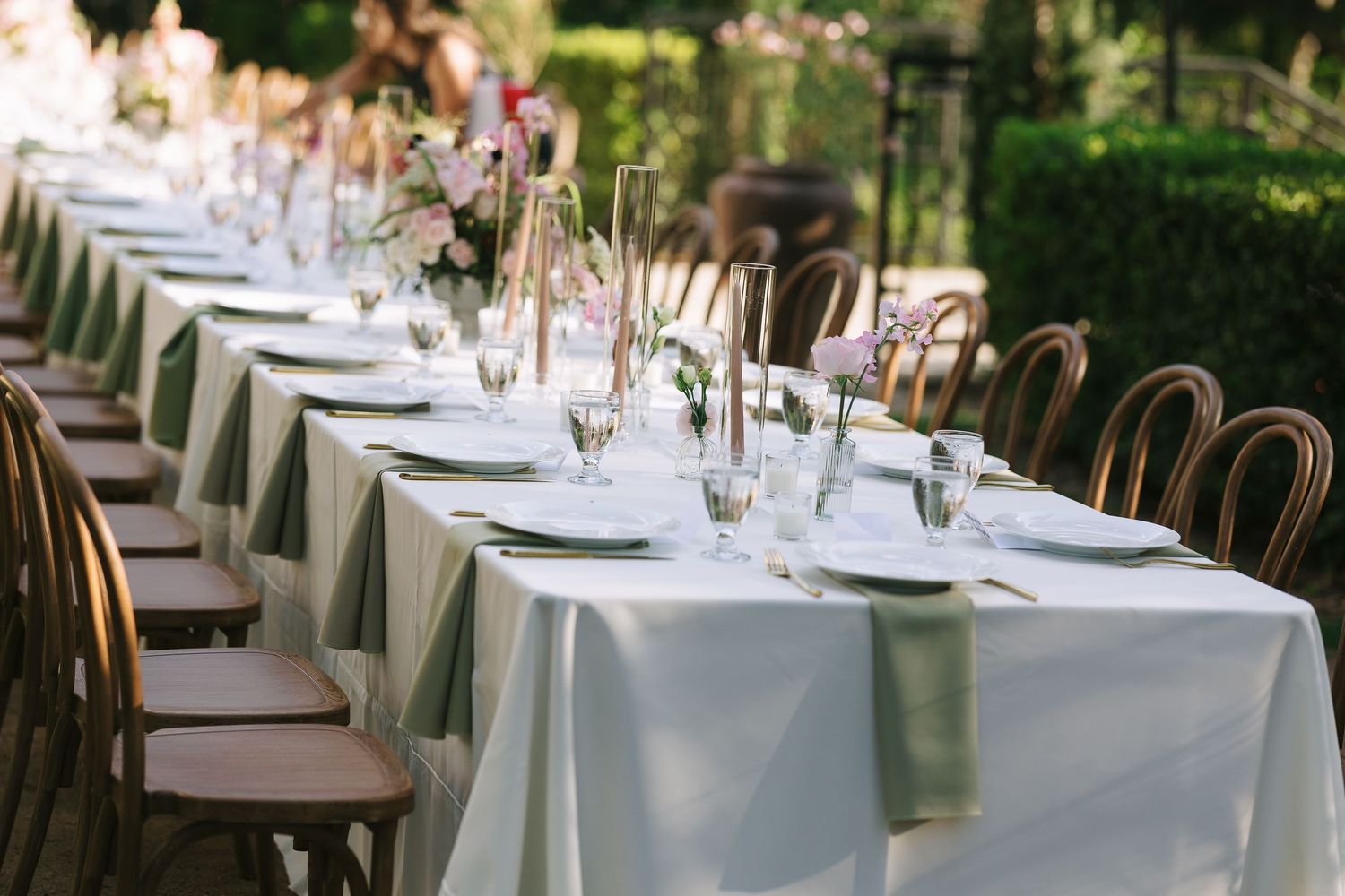Long banquet tables set with white linens and delicate floral centerpieces for an outdoor wedding reception.