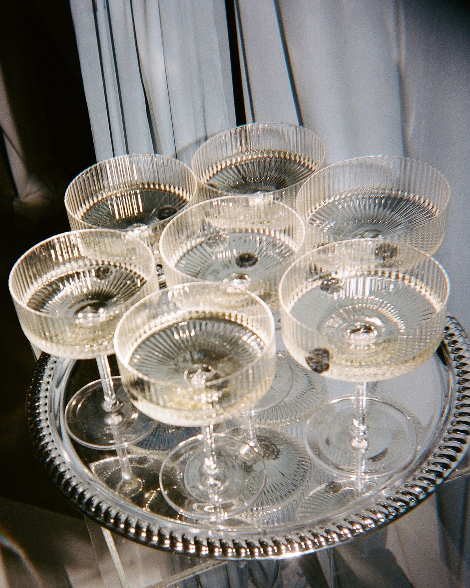 Eight ribbed crystal coupe glasses filled with champagne arranged on a silver beaded tray.