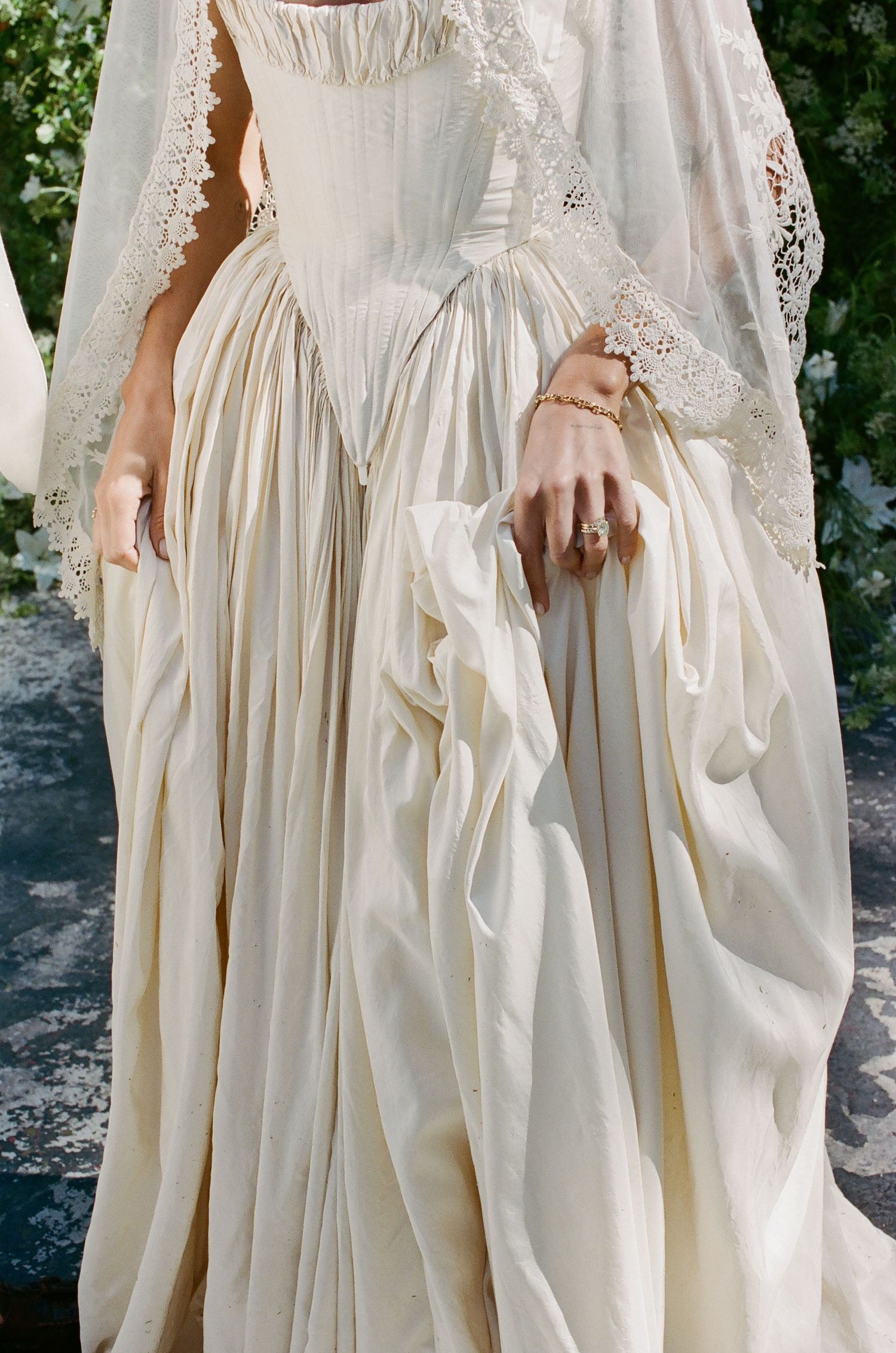 Elegant ivory wedding gown with corset bodice, voluminous skirt, and lace veil, accessorized with gold rings.