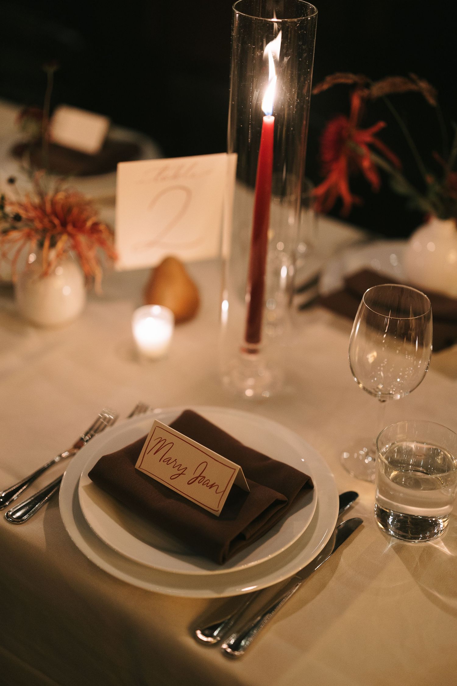Elegant place settings at a formal dinner with candlelight and name cards on dark plates.