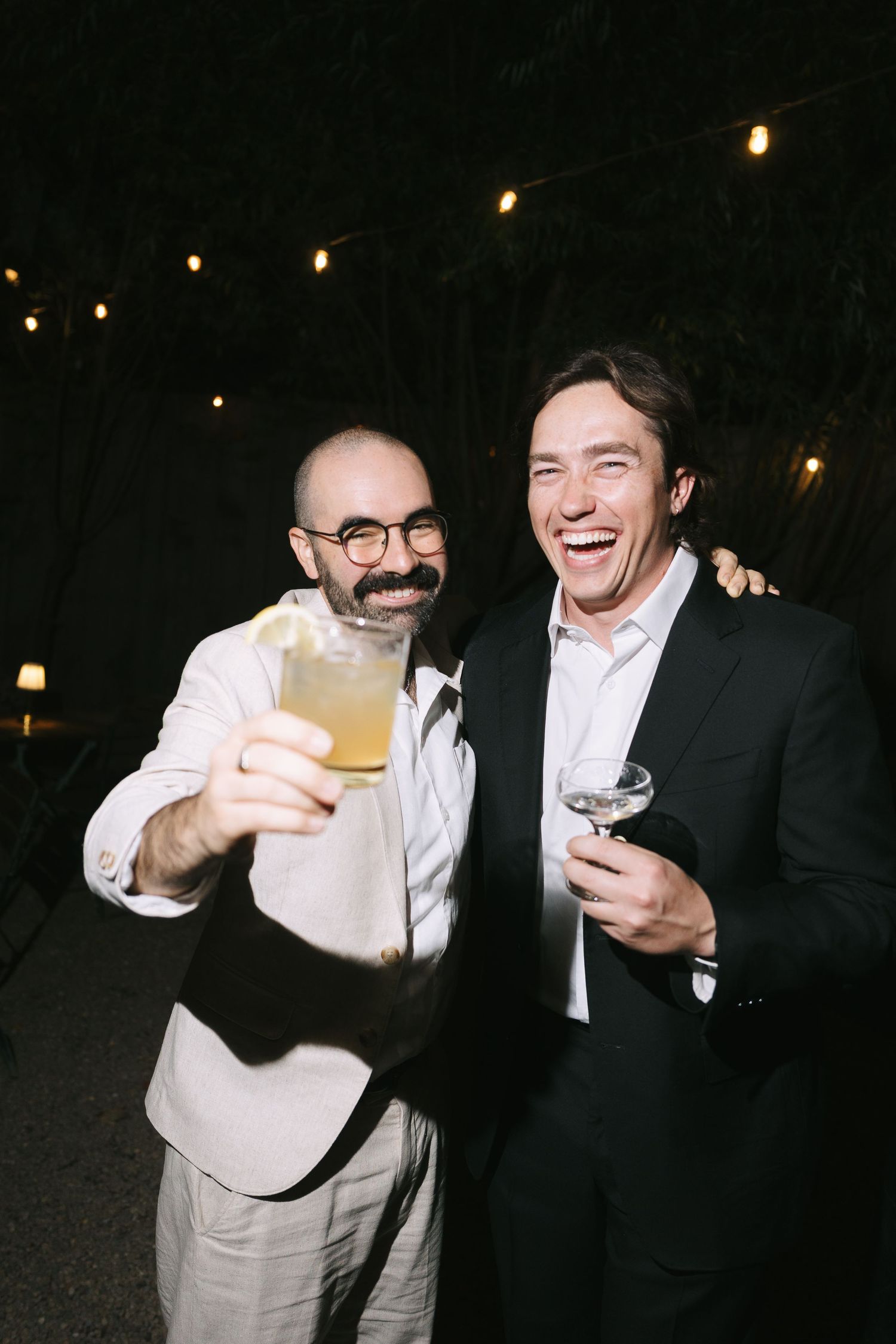 Two guests in formal attire sharing drinks and laughs at an evening celebration.